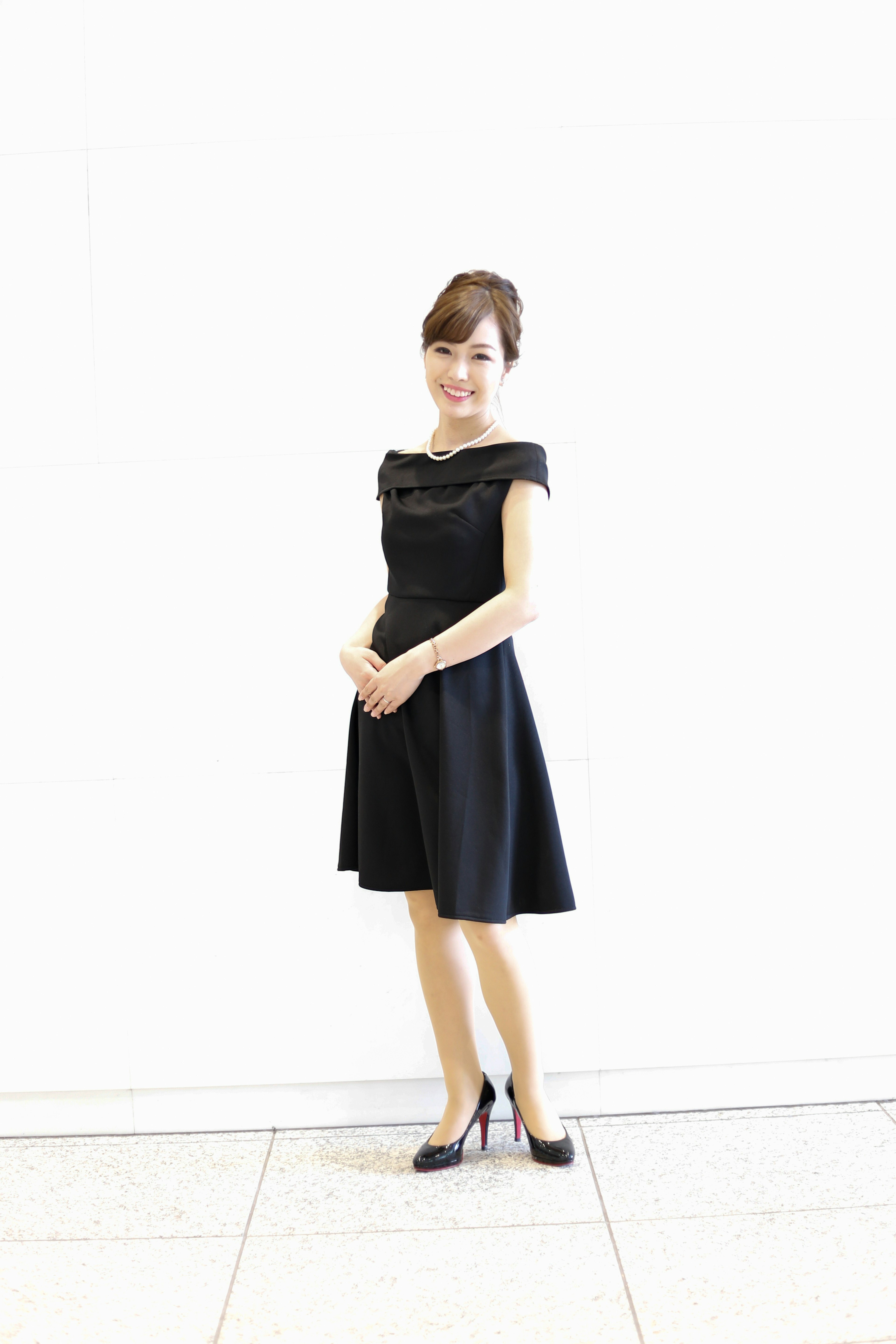 A woman in a black dress stands in front of a white background