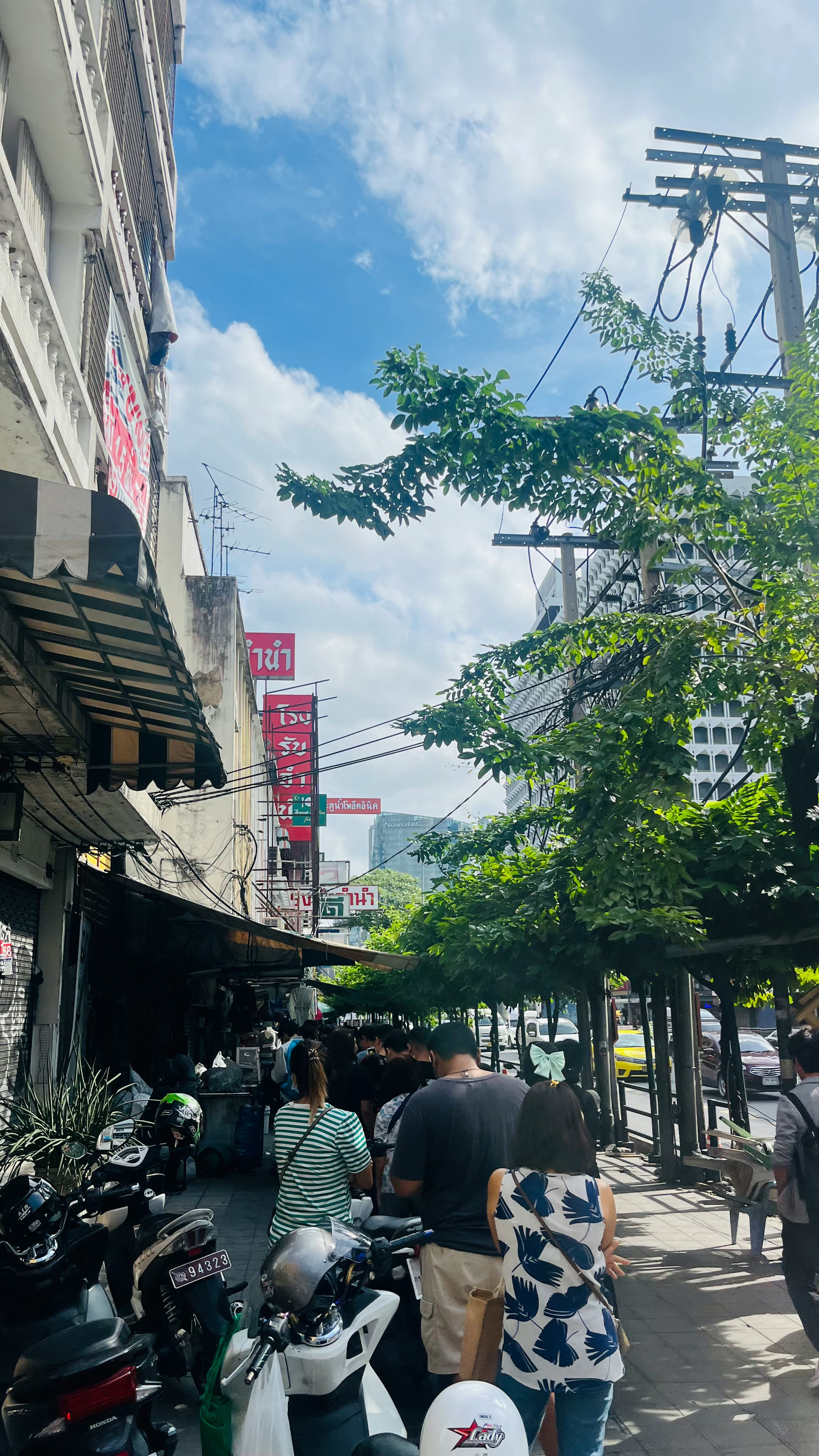 Pemandangan jalan luar ruangan dengan orang-orang antre di restoran di bawah langit biru