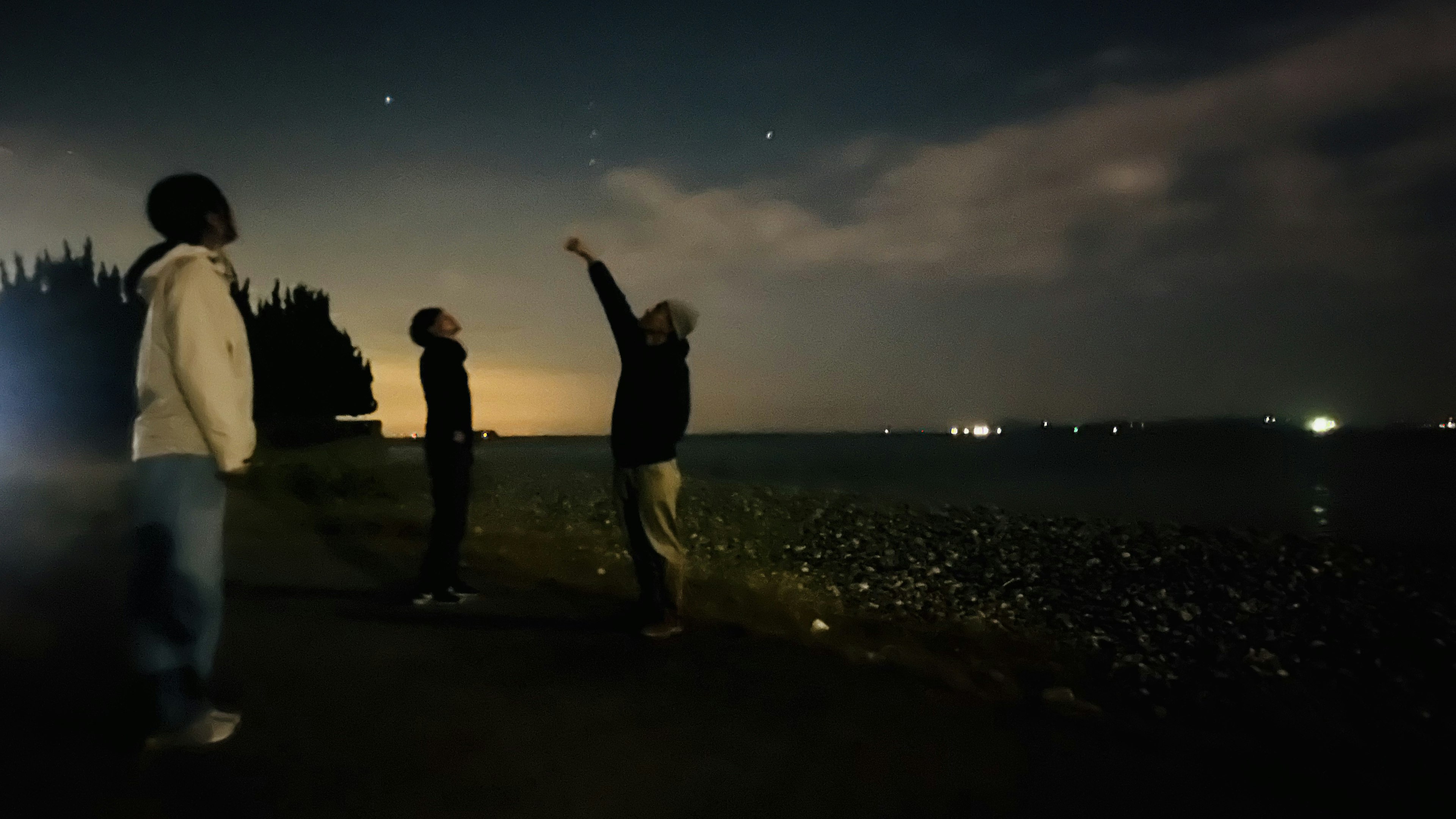 夜空を見上げる三人の人物と星々のある風景