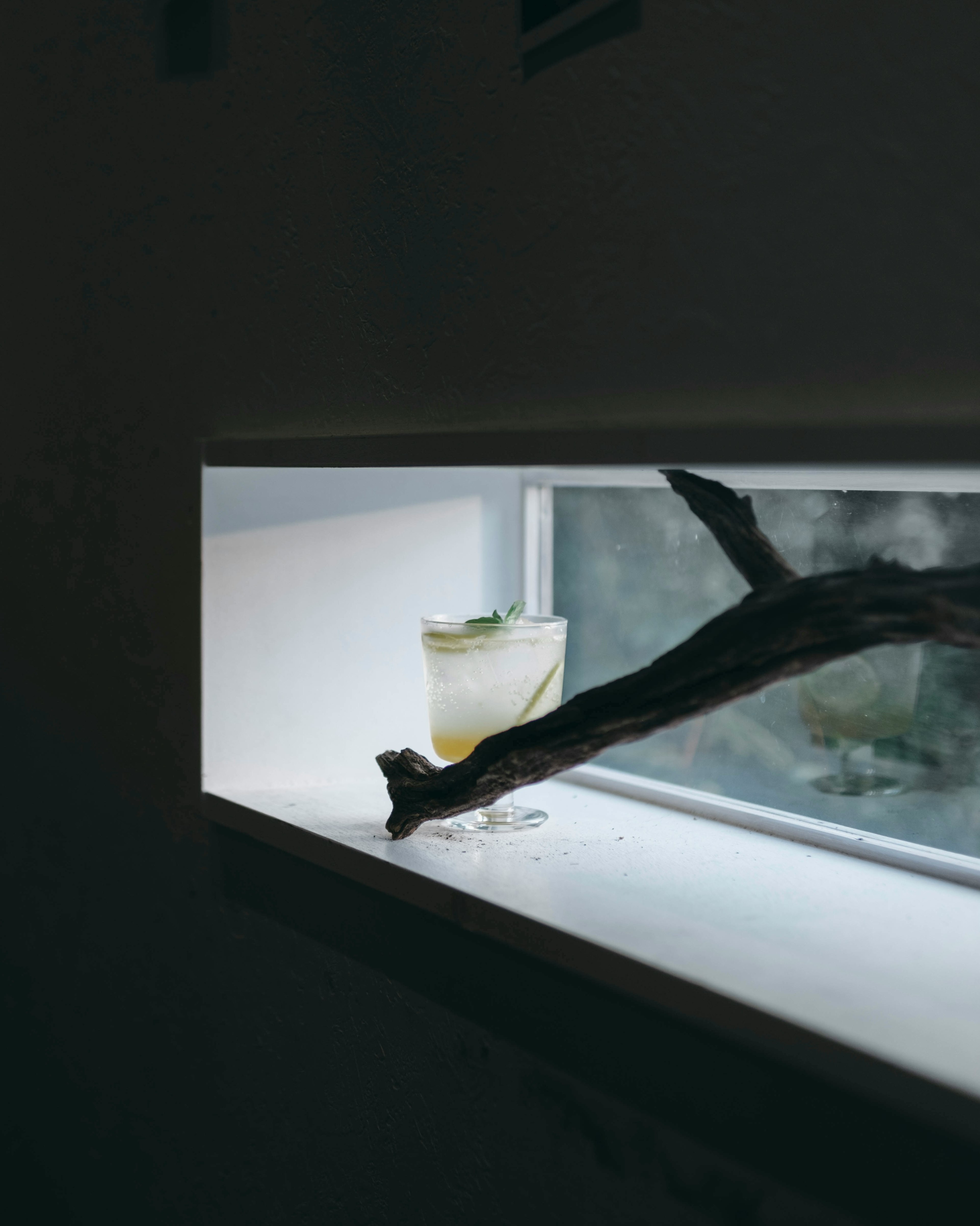 A cocktail glass placed on a bright windowsill with a natural branch