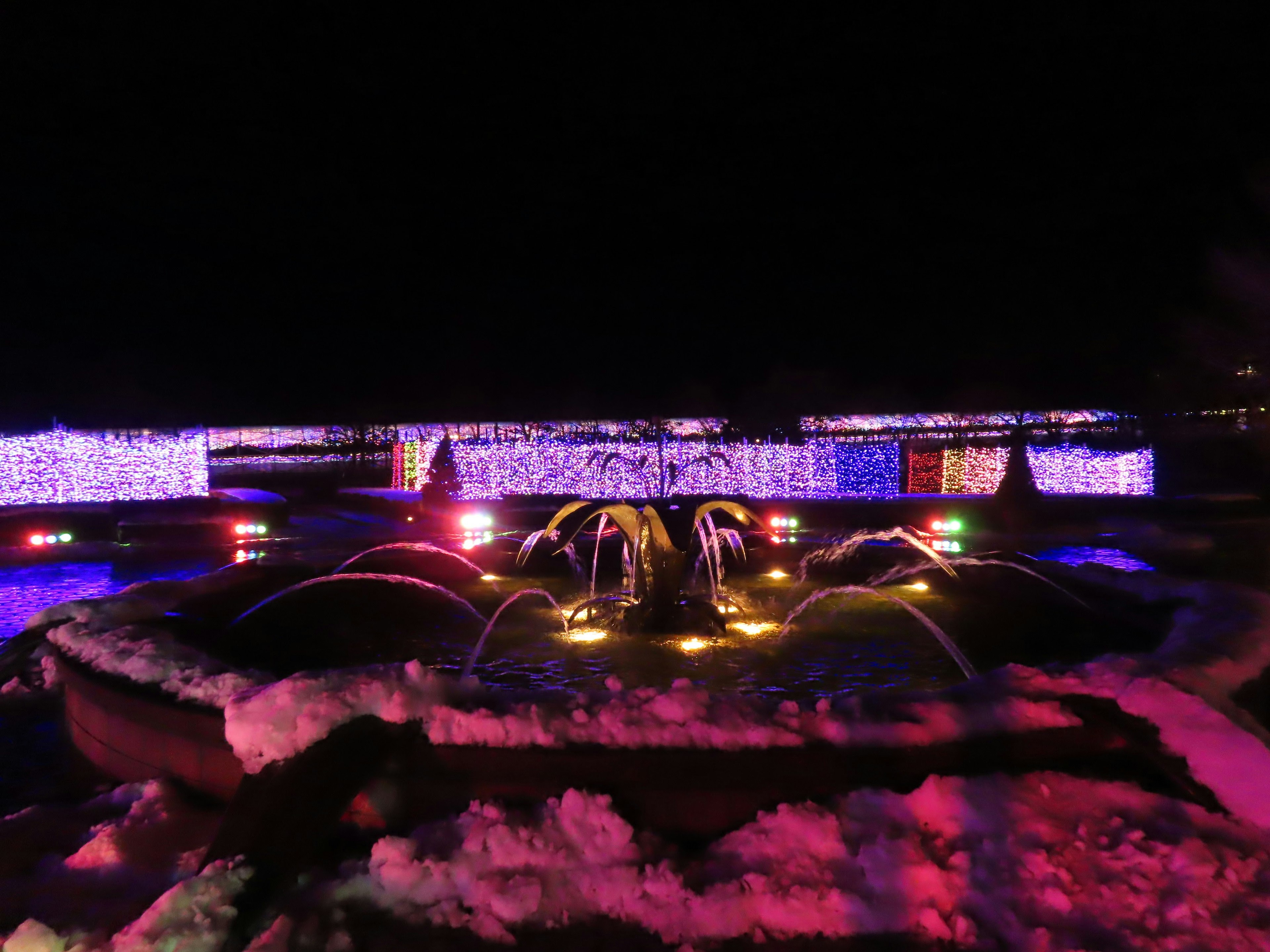 Fontana illuminata con luci colorate in un paesaggio innevato di notte