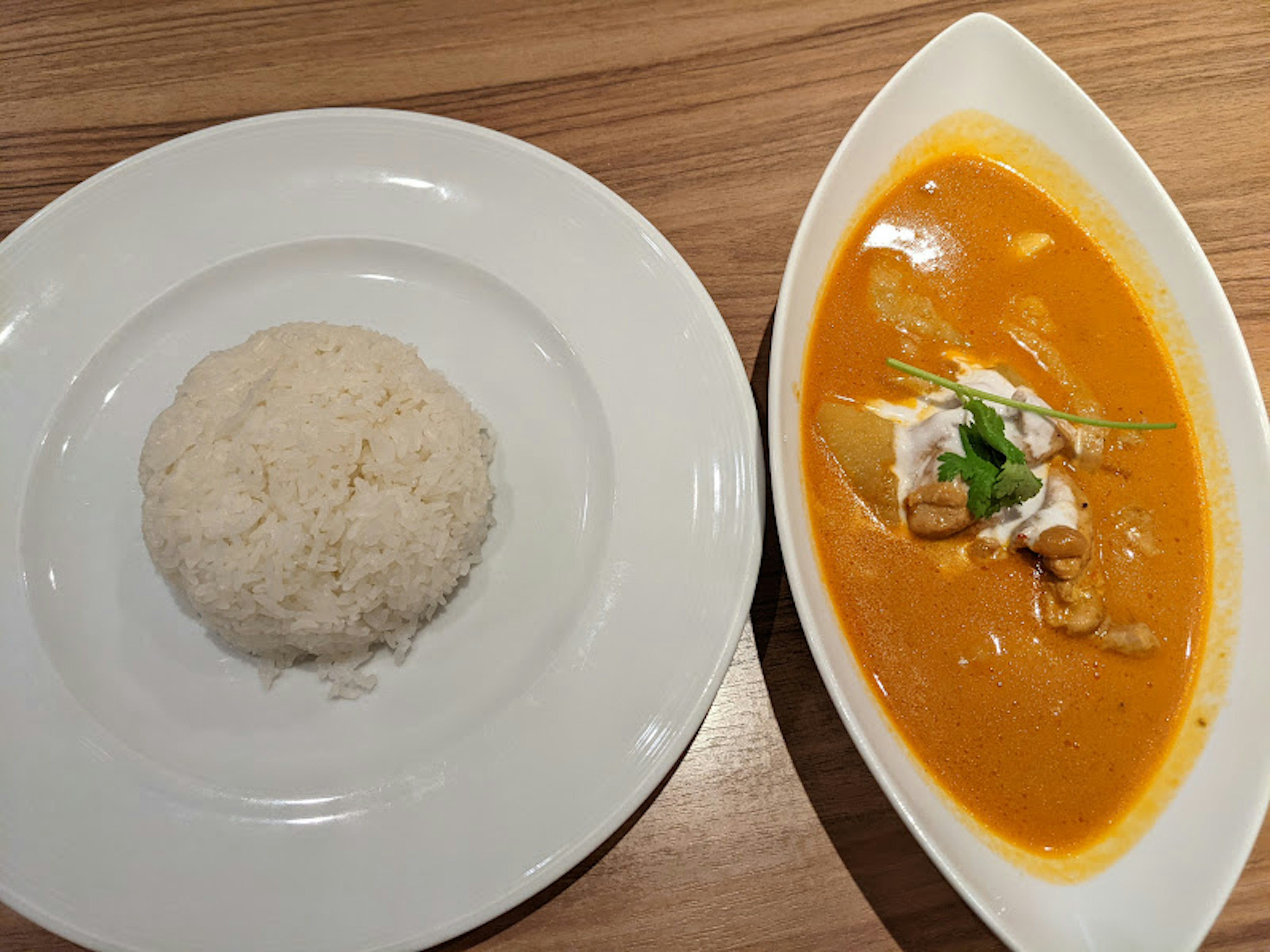 Piring nasi putih di samping mangkuk kari oranye yang dihiasi dengan rempah