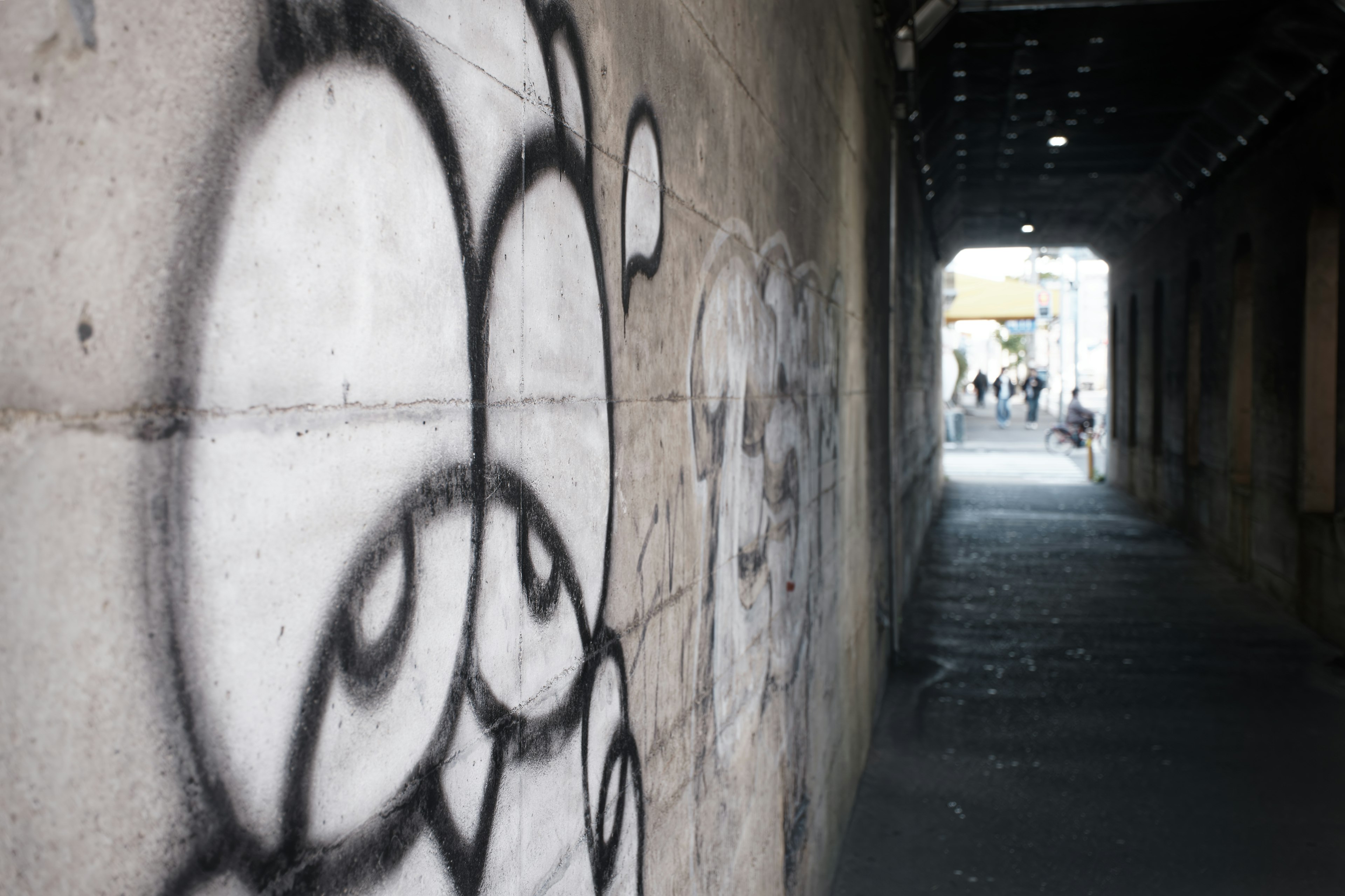 Schmale Gasse mit Graffiti an der Wand und Menschen in der Ferne