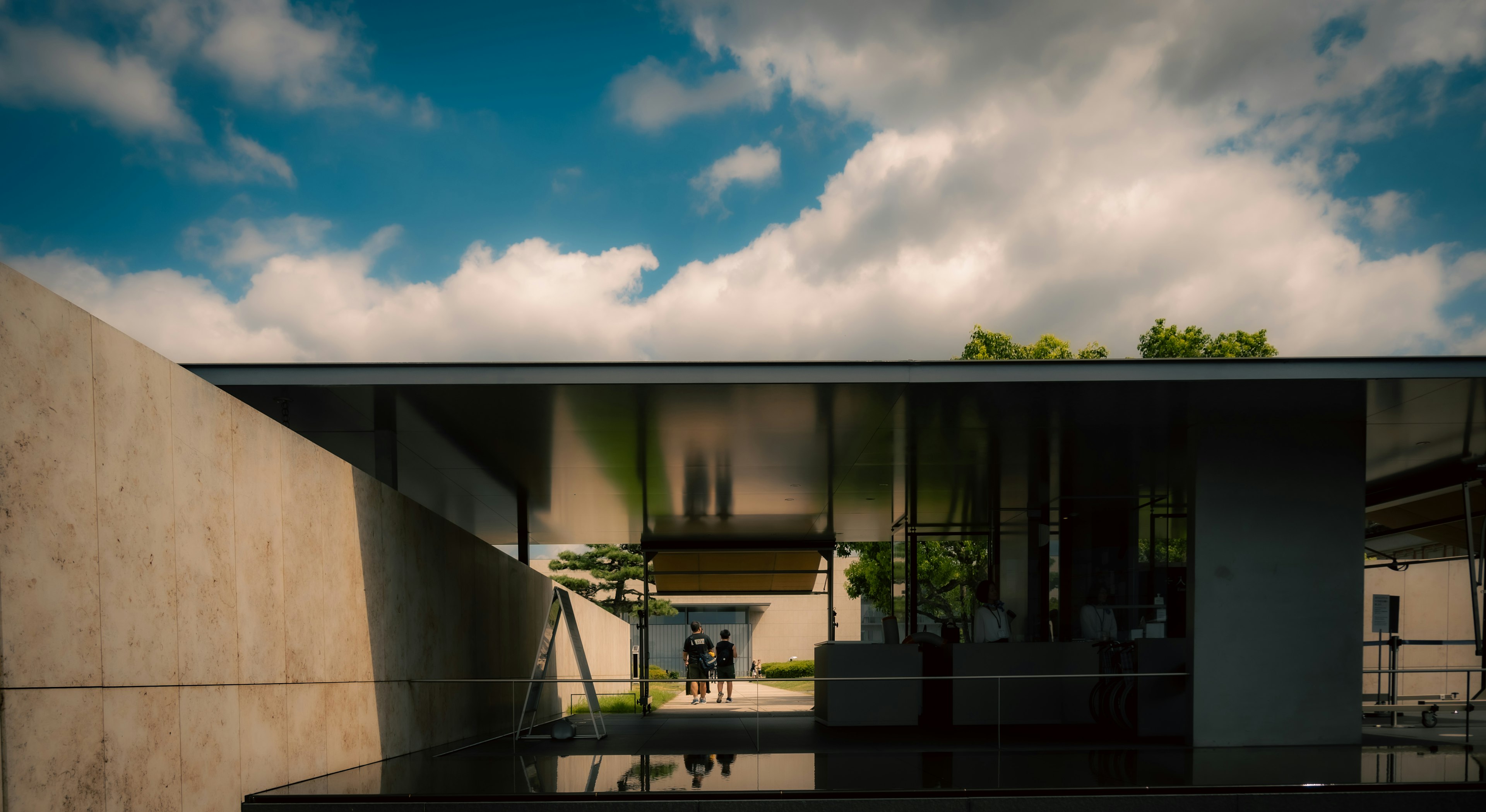 Modern building exterior with glass facade and greenery, blue sky and clouds in the background