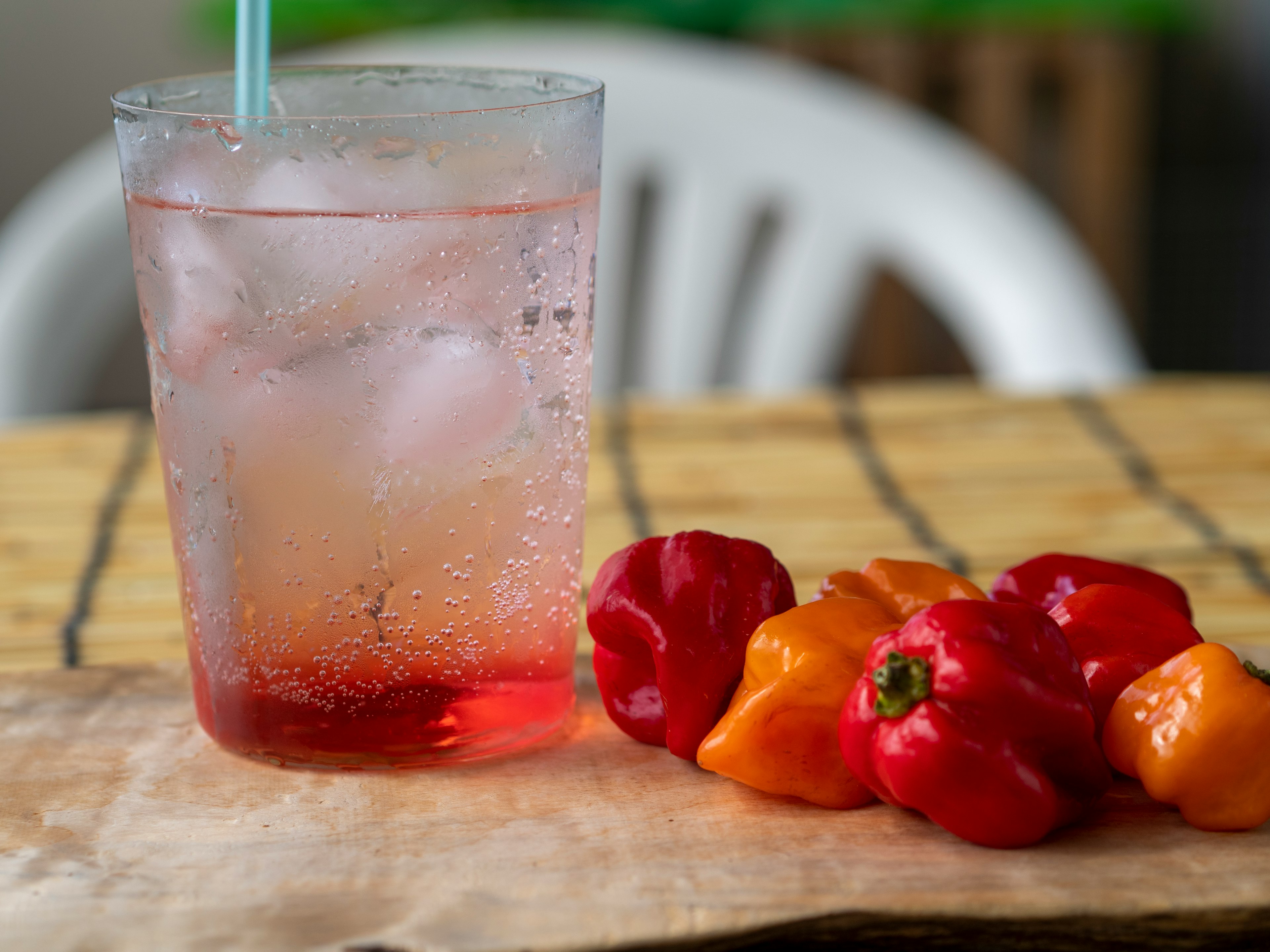 Un vaso de bebida gaseosa con hielo junto a pimientos rojos y naranjas sobre una mesa de madera