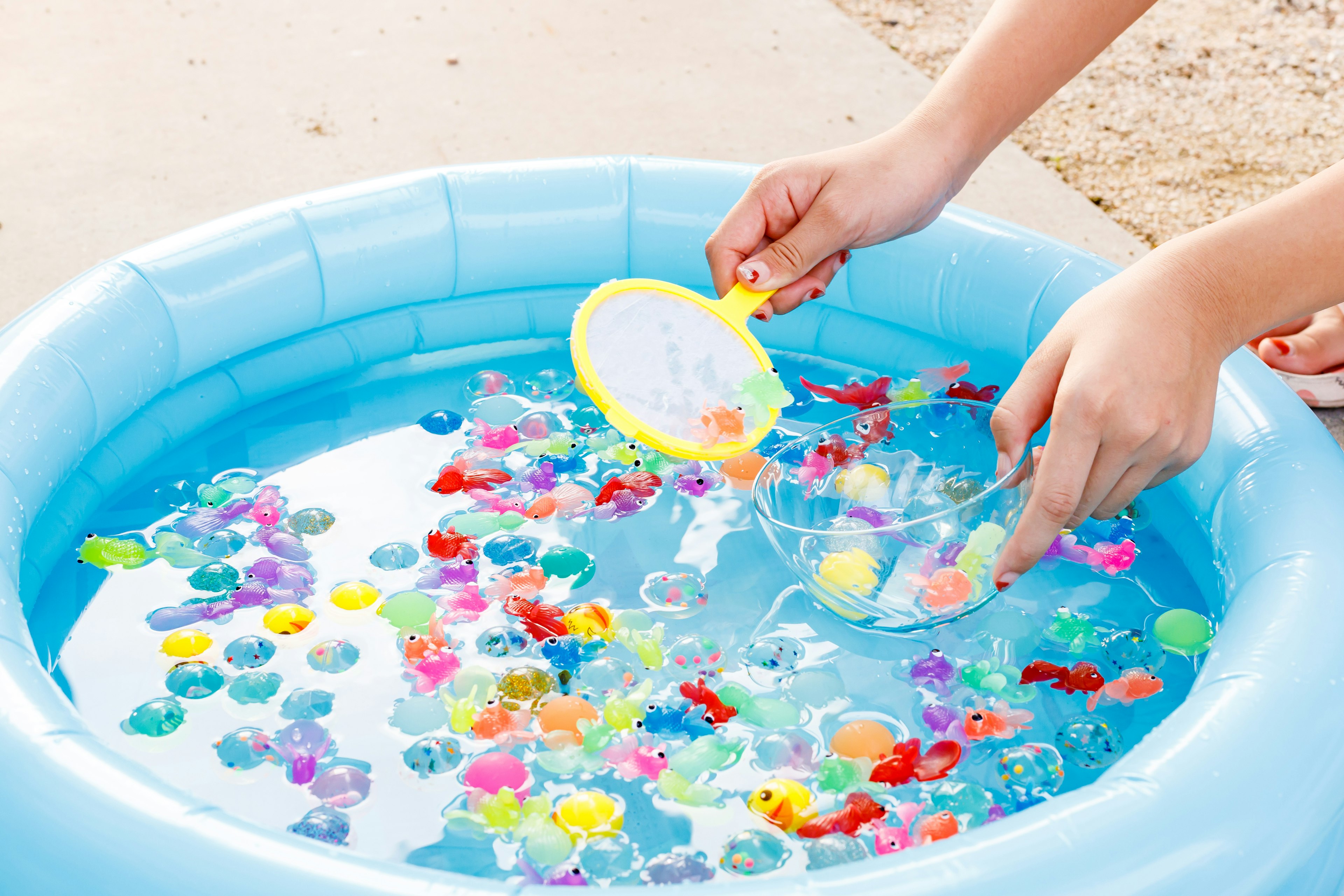 Hände, die bunte Perlen aus einem blauen aufblasbaren Pool mit Wasser schöpfen