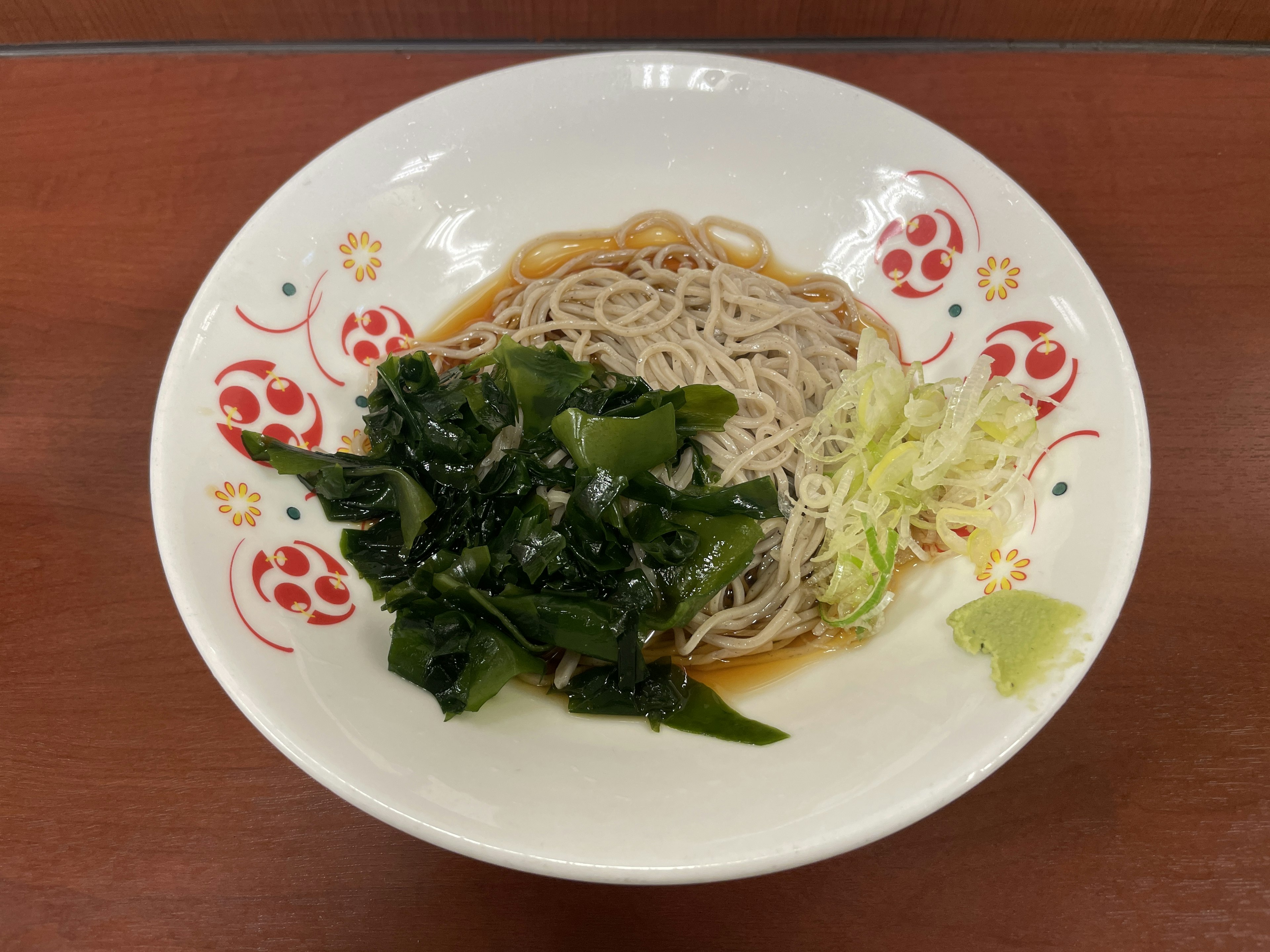 A plate of soba noodles with seaweed salad and green vegetables