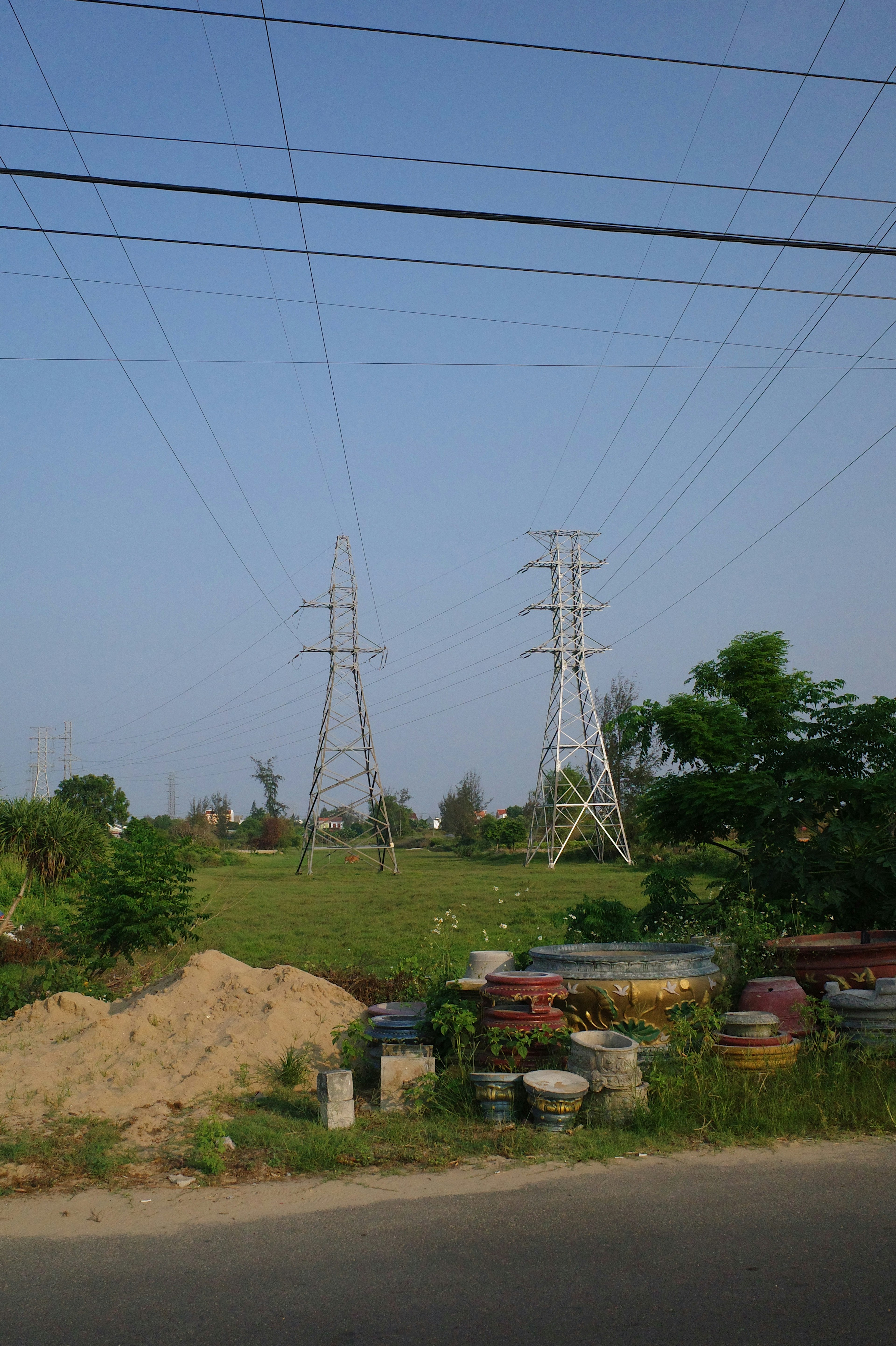 Landschaft mit Hochspannungsleitungen und -masten, Grasland und einem Erdhügel