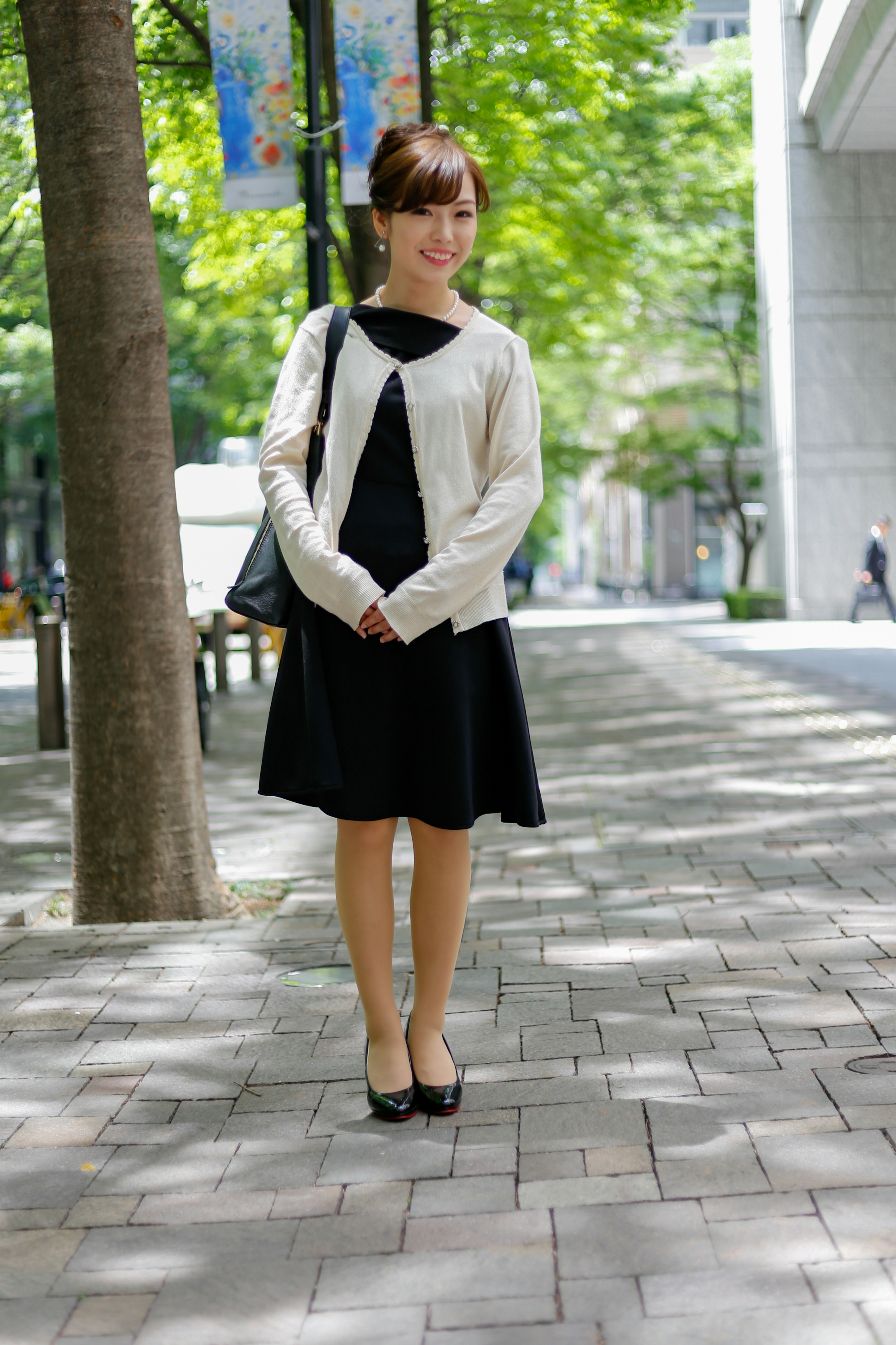 Woman in black dress and white cardigan standing on a city street