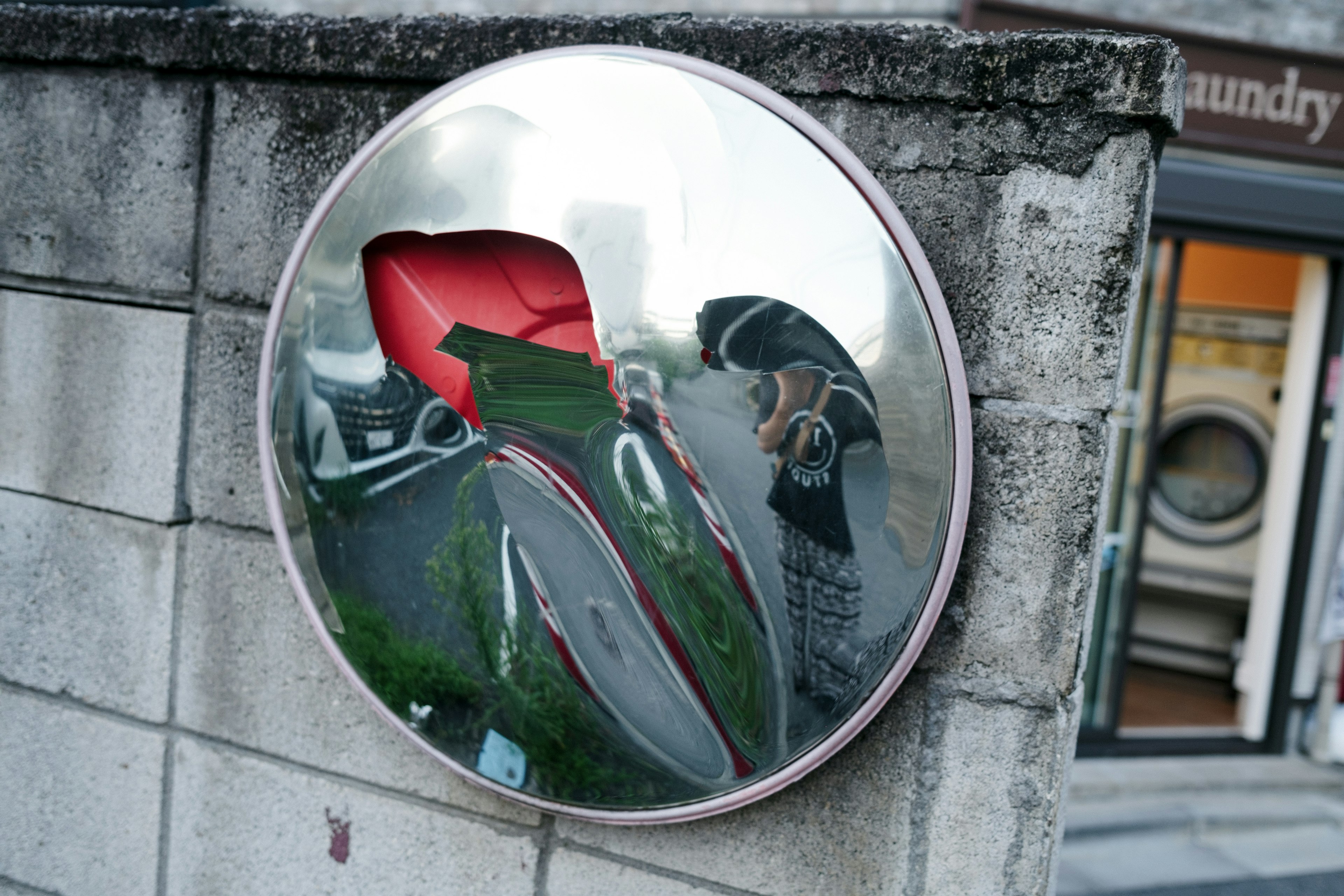 Un objeto circular reflectante montado en una pared que muestra el paisaje circundante con una sección roja prominente