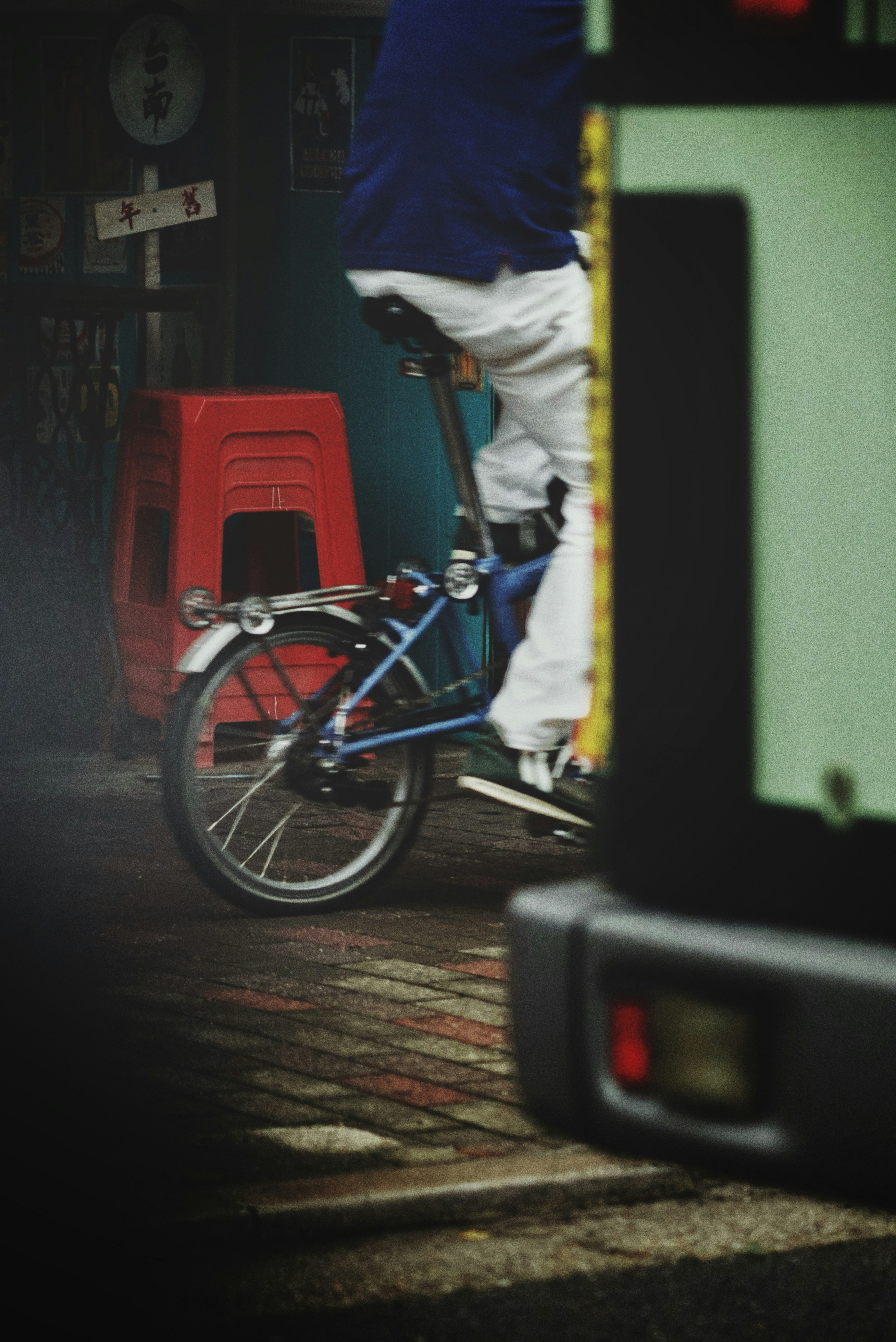 A person riding a bicycle with a blurred background featuring a green vehicle and orange cones