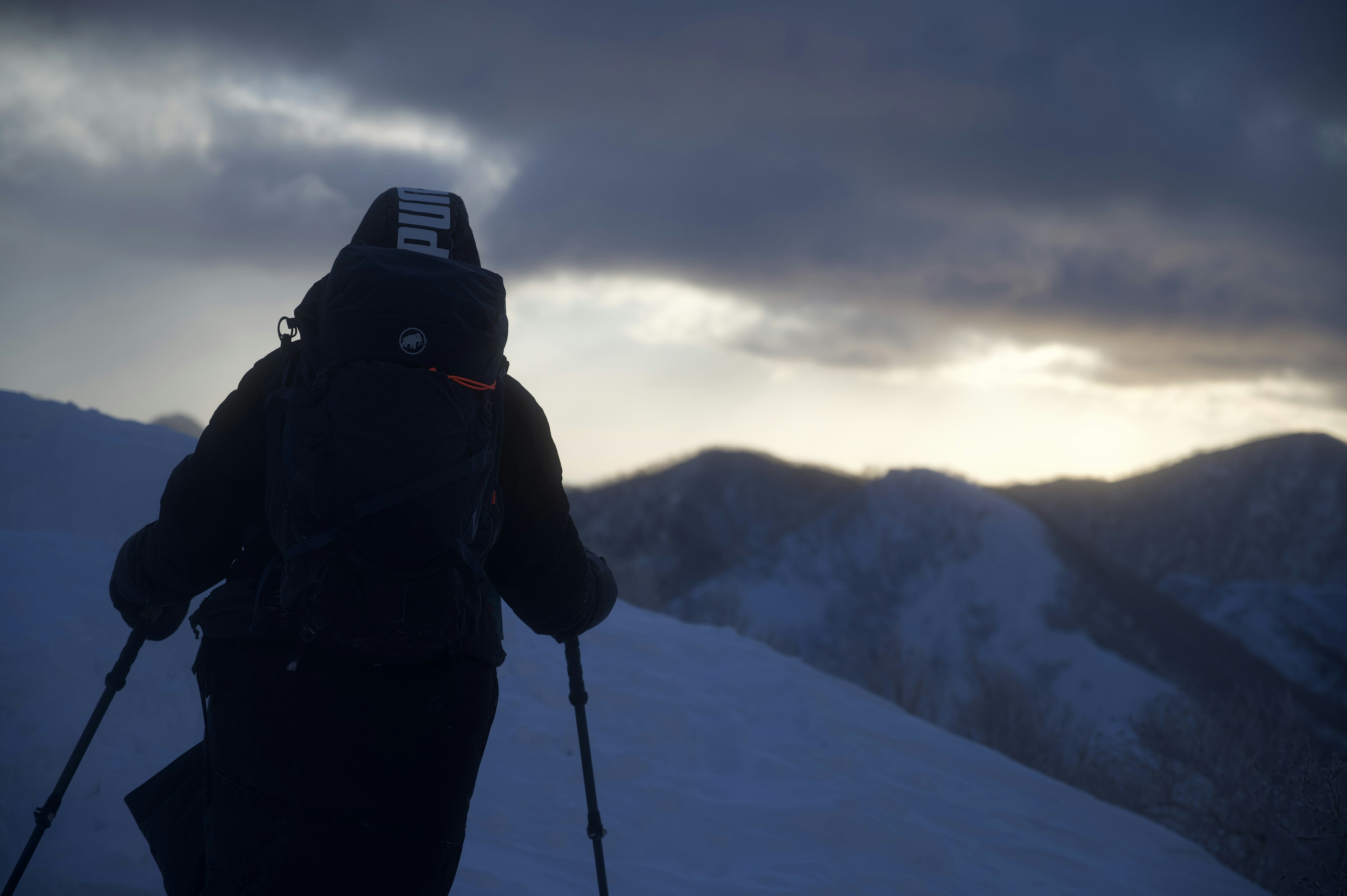 Silhouette of a person hiking against a snowy mountain backdrop