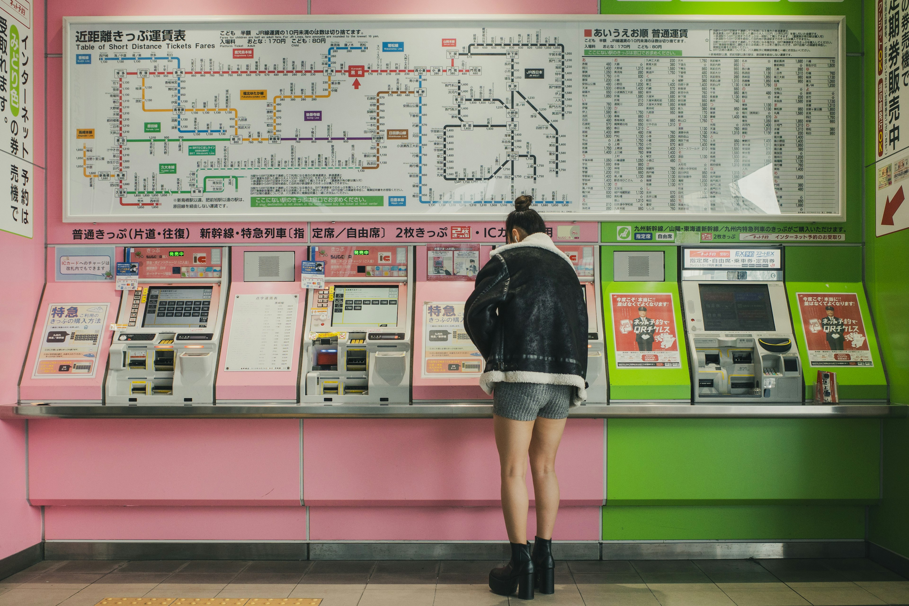 女性站在票務機前，背景為粉色和綠色牆壁