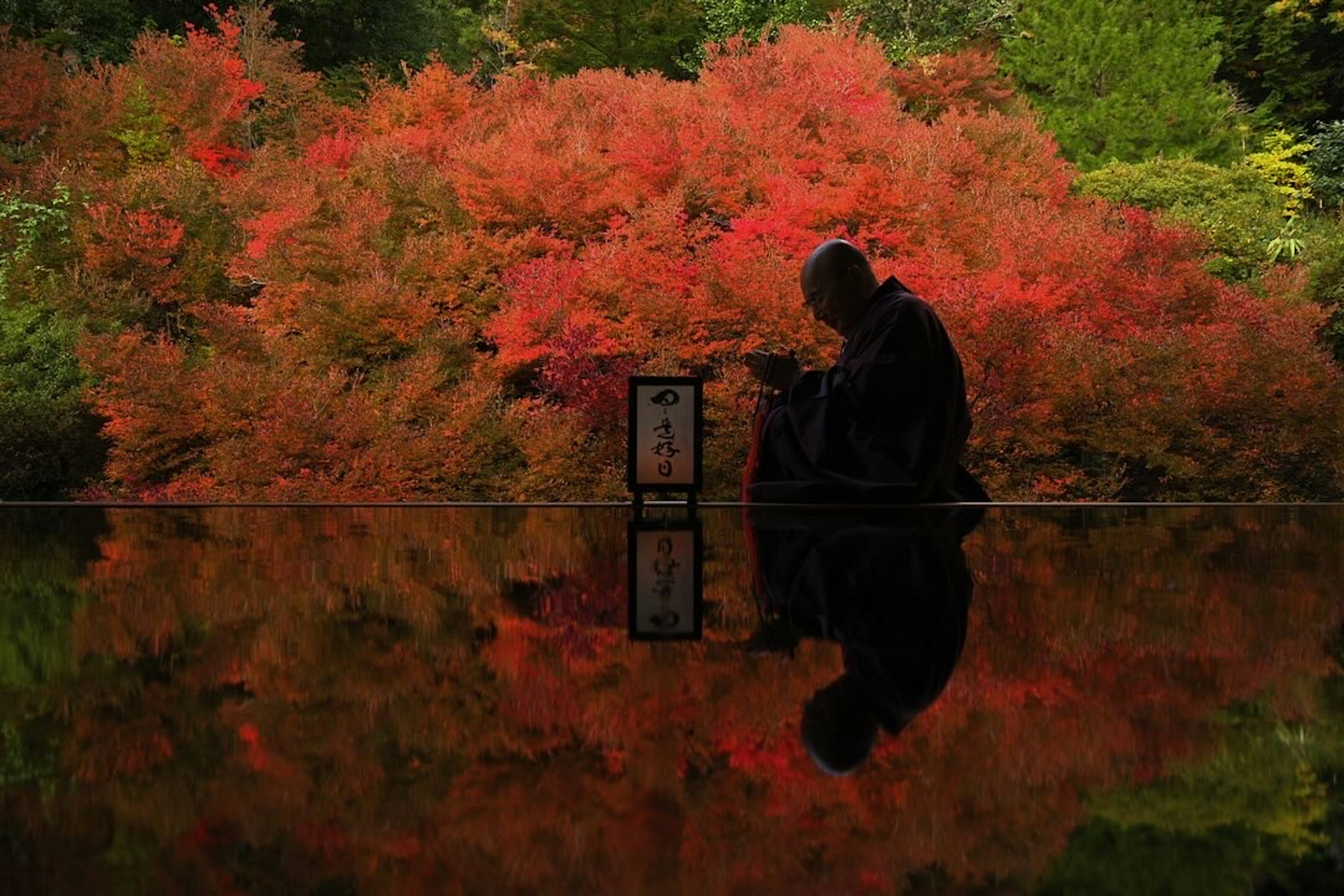 Silhouette eines Mönchs, der ruhig vor einem Hintergrund aus lebhaftem Herbstlaub sitzt