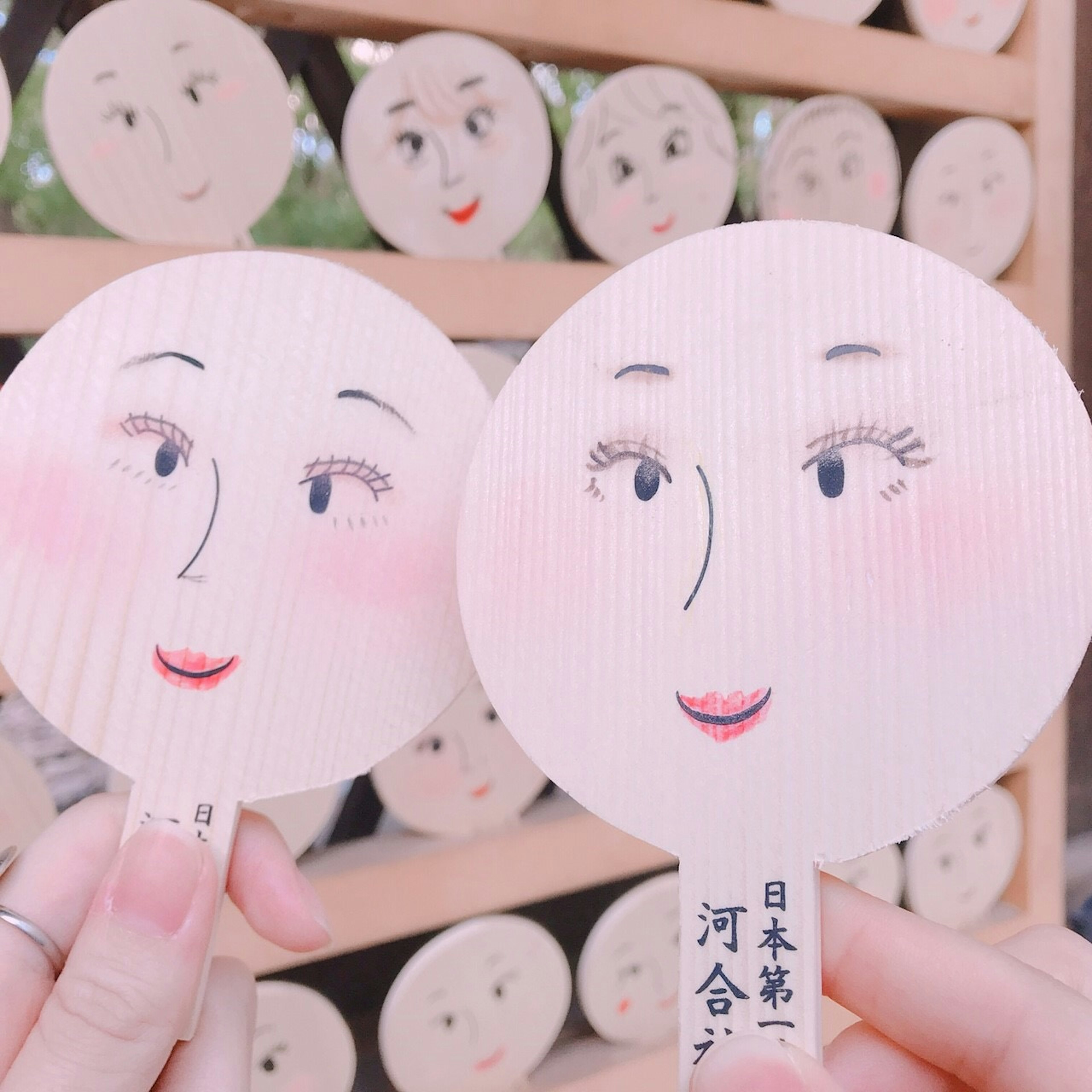 Two hand-held fans with painted faces in front of a background of more fans