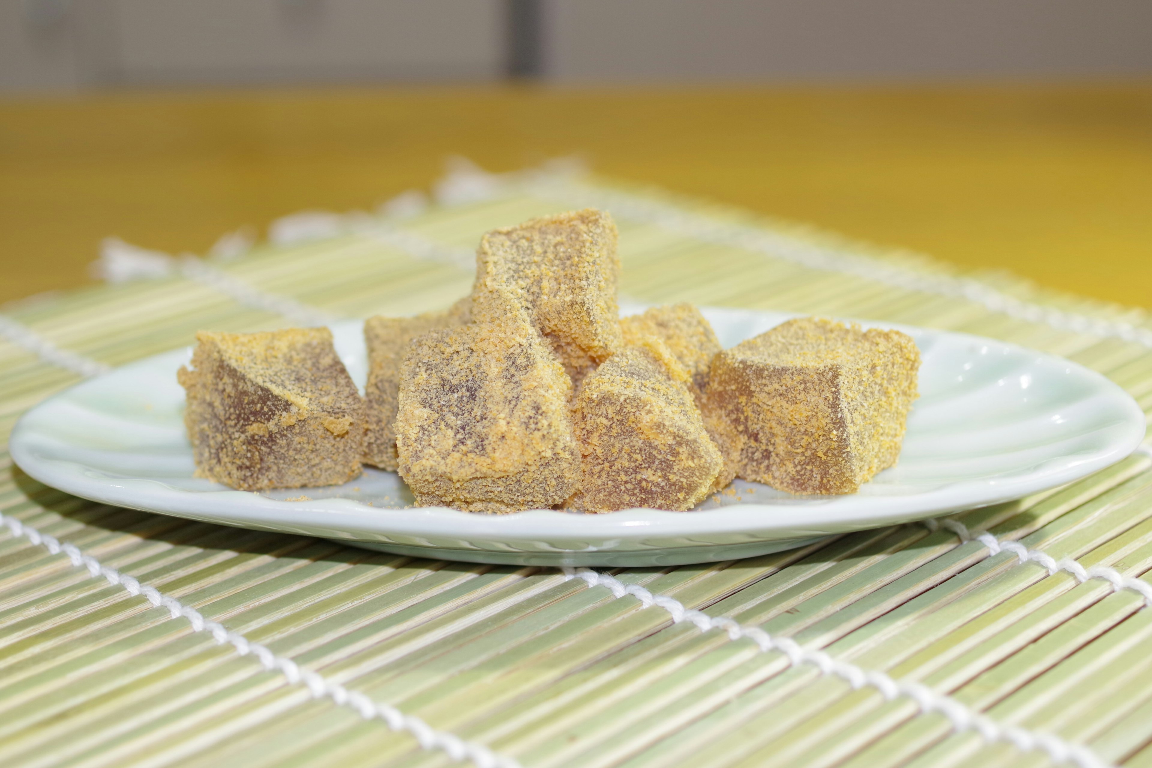 Cubes de sucre brun sur une assiette blanche disposés sur un tapis en bambou