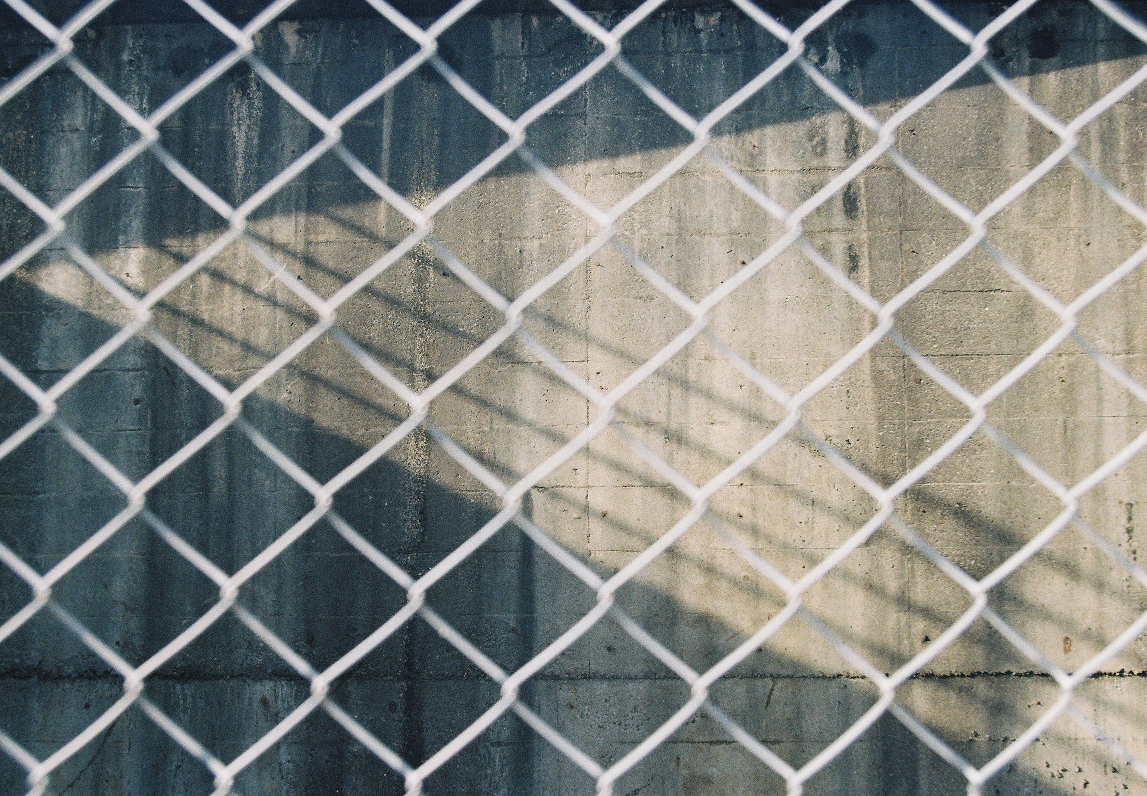 Ombre et texture d'un mur vues à travers une clôture en treillis métallique