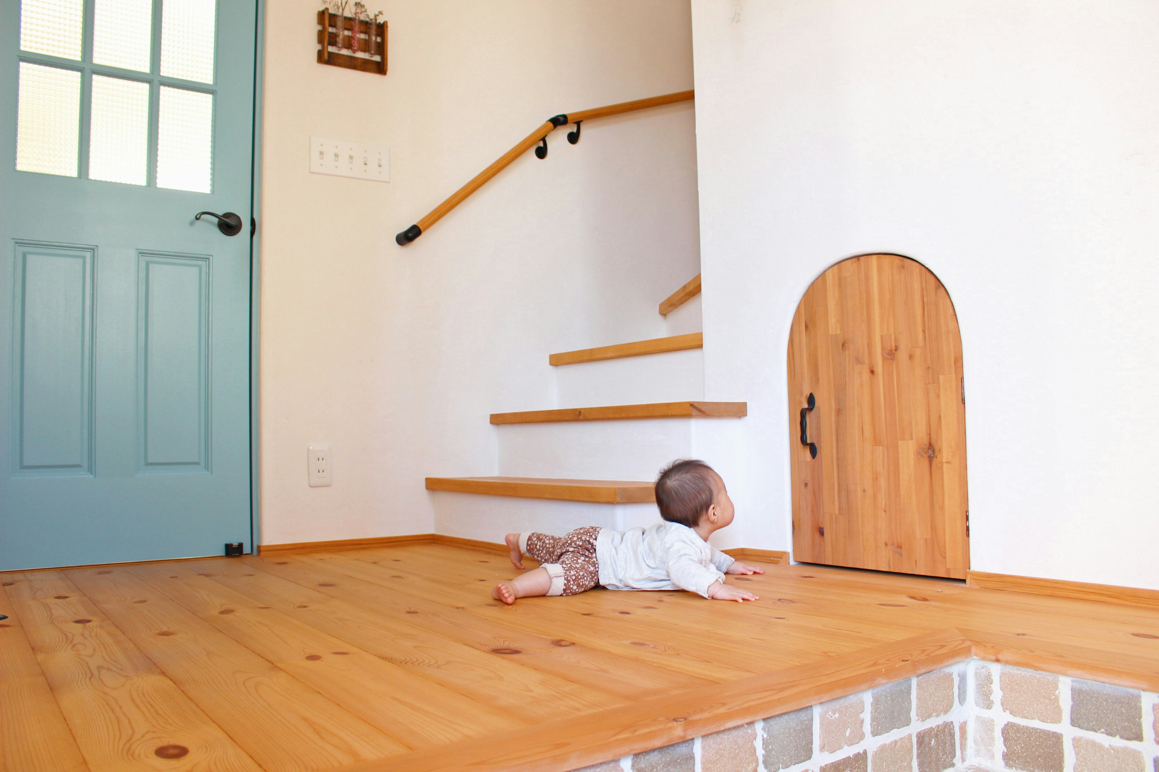 A baby crawling towards a small door and stairs in a bright indoor setting