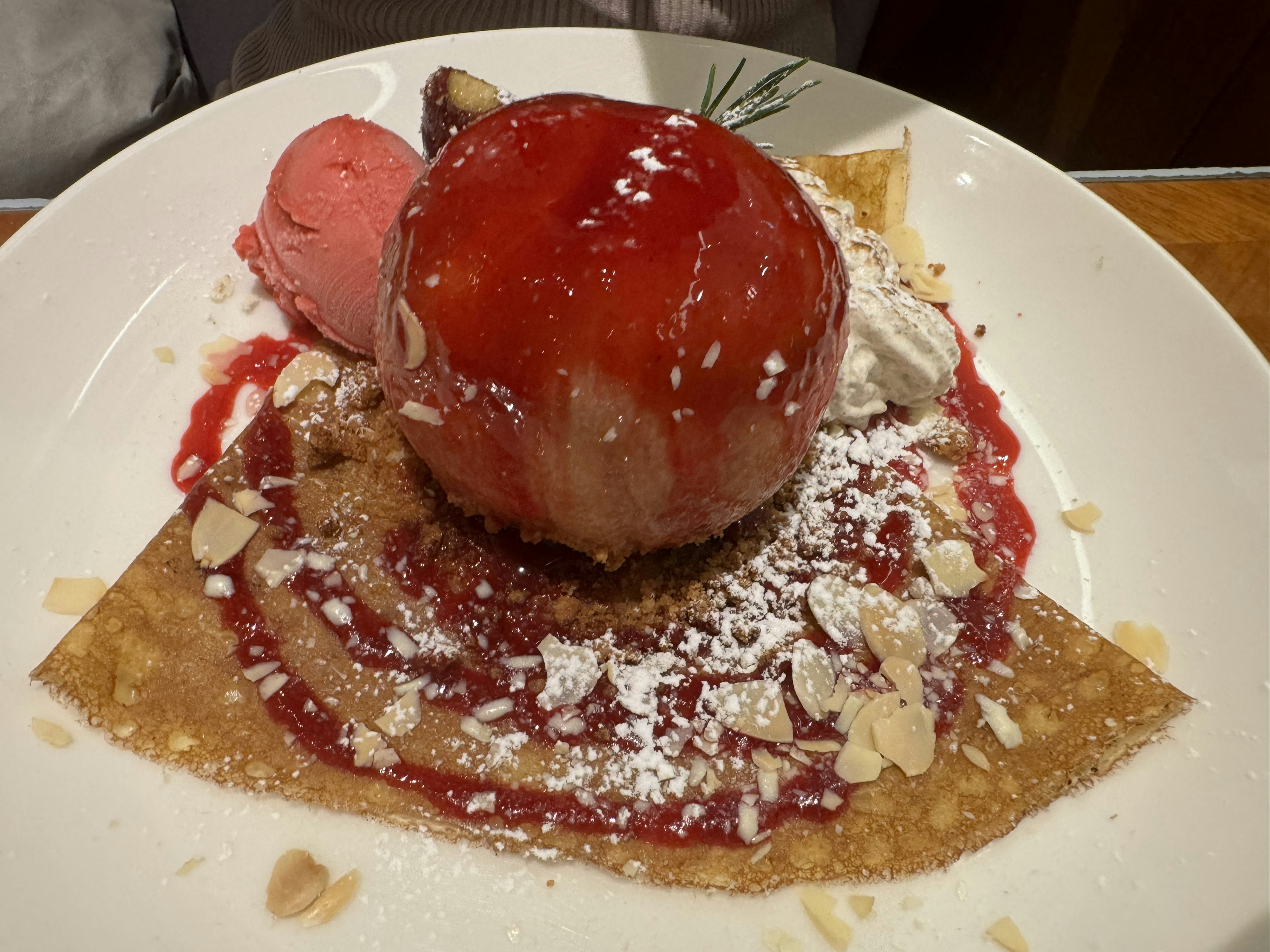 Dessert featuring a red apple ice cream atop a crepe with raspberry sauce and almonds