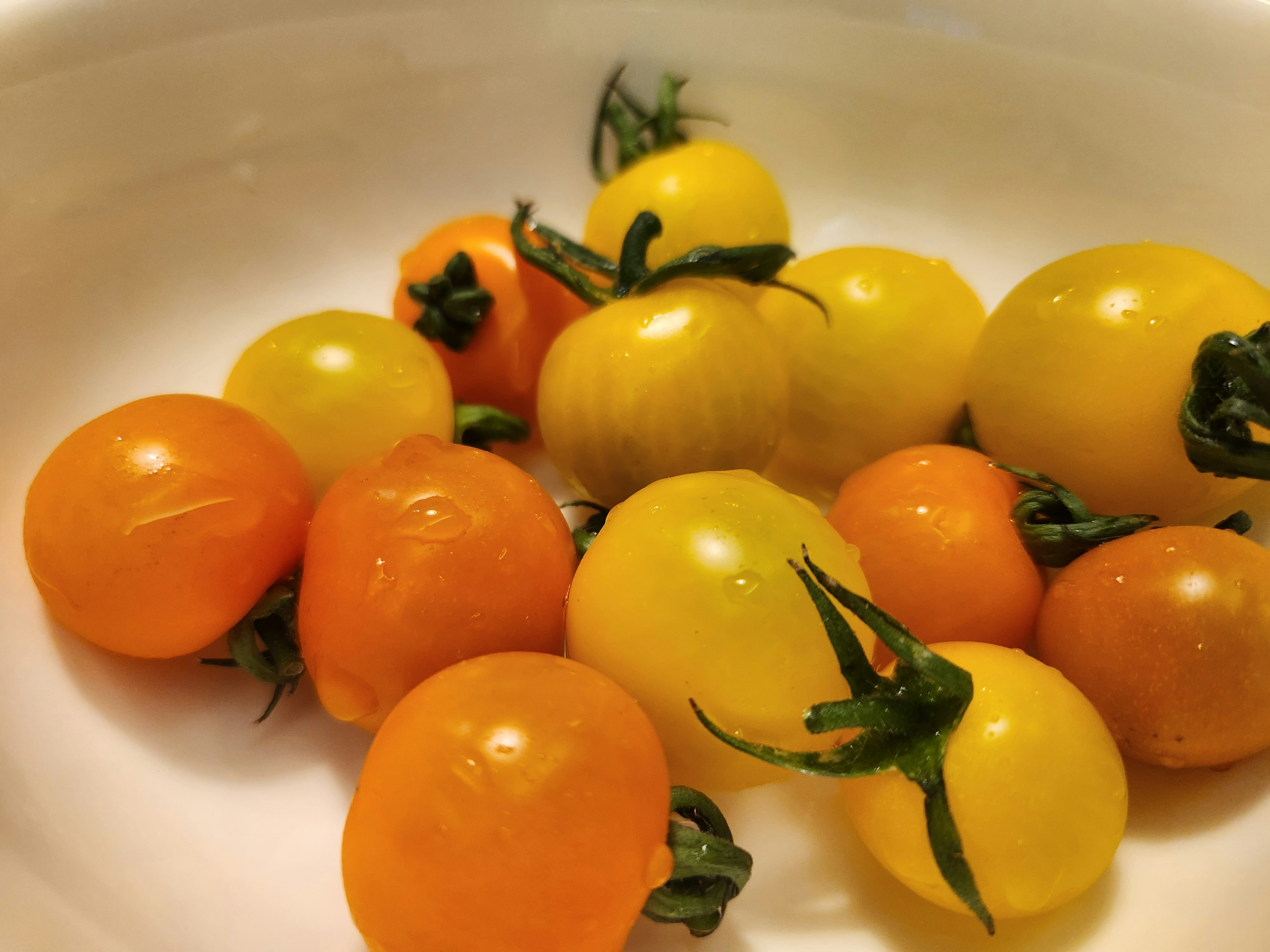 Small yellow and orange cherry tomatoes arranged in a white bowl