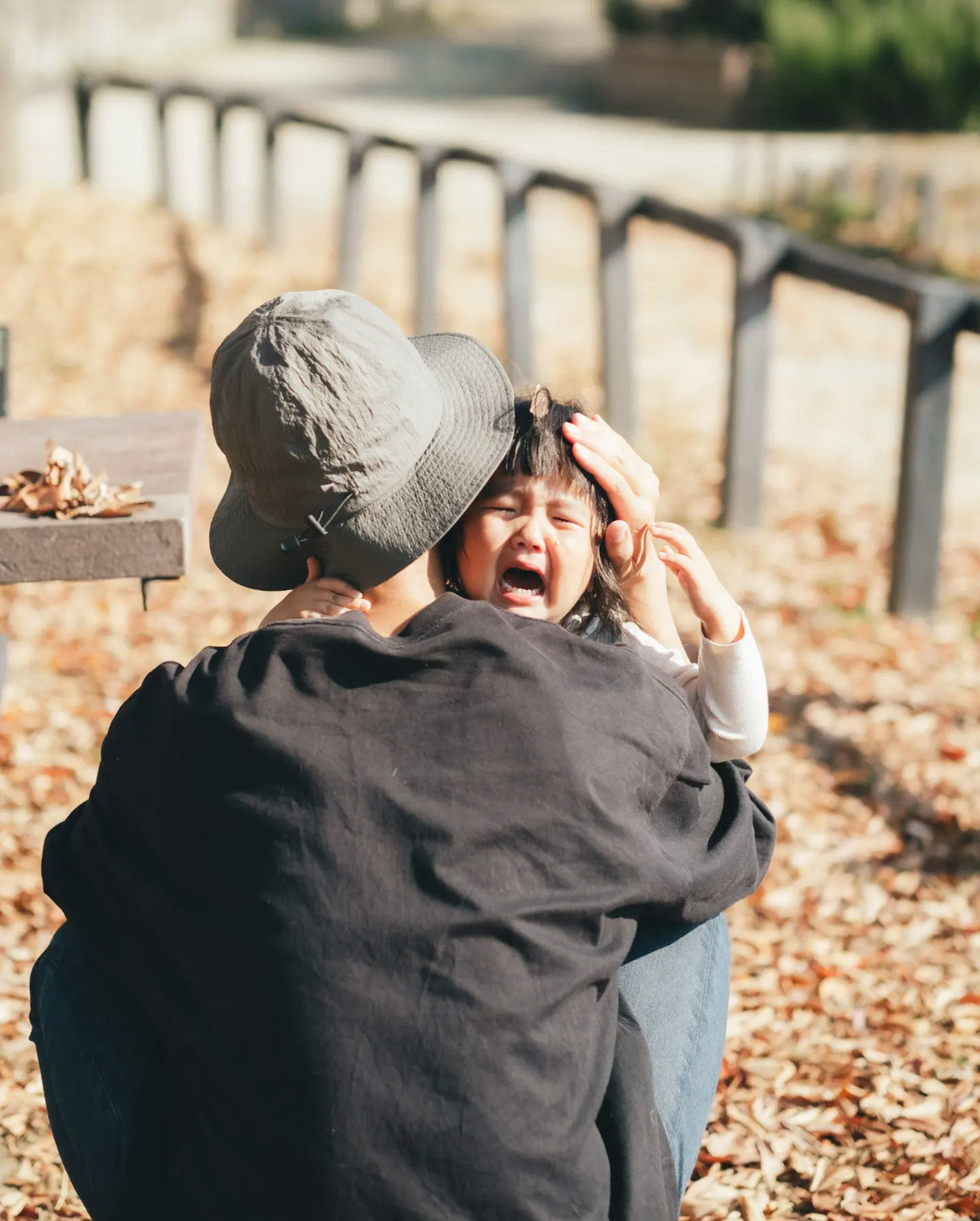 Une scène dans un parc d'automne montrant un enfant qui pleure tandis qu'un adulte le réconforte