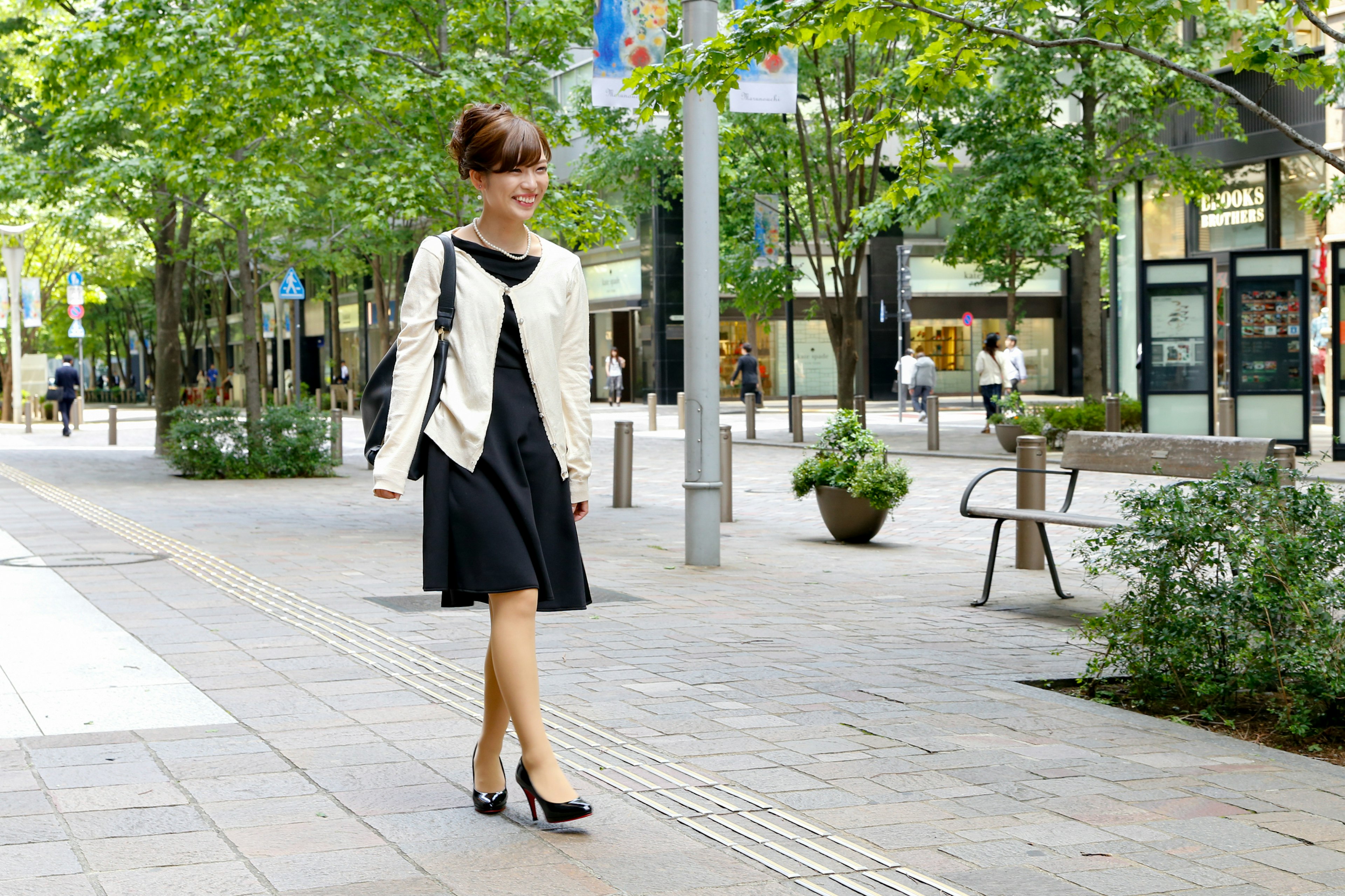 Woman in black dress and white jacket walking in an urban setting