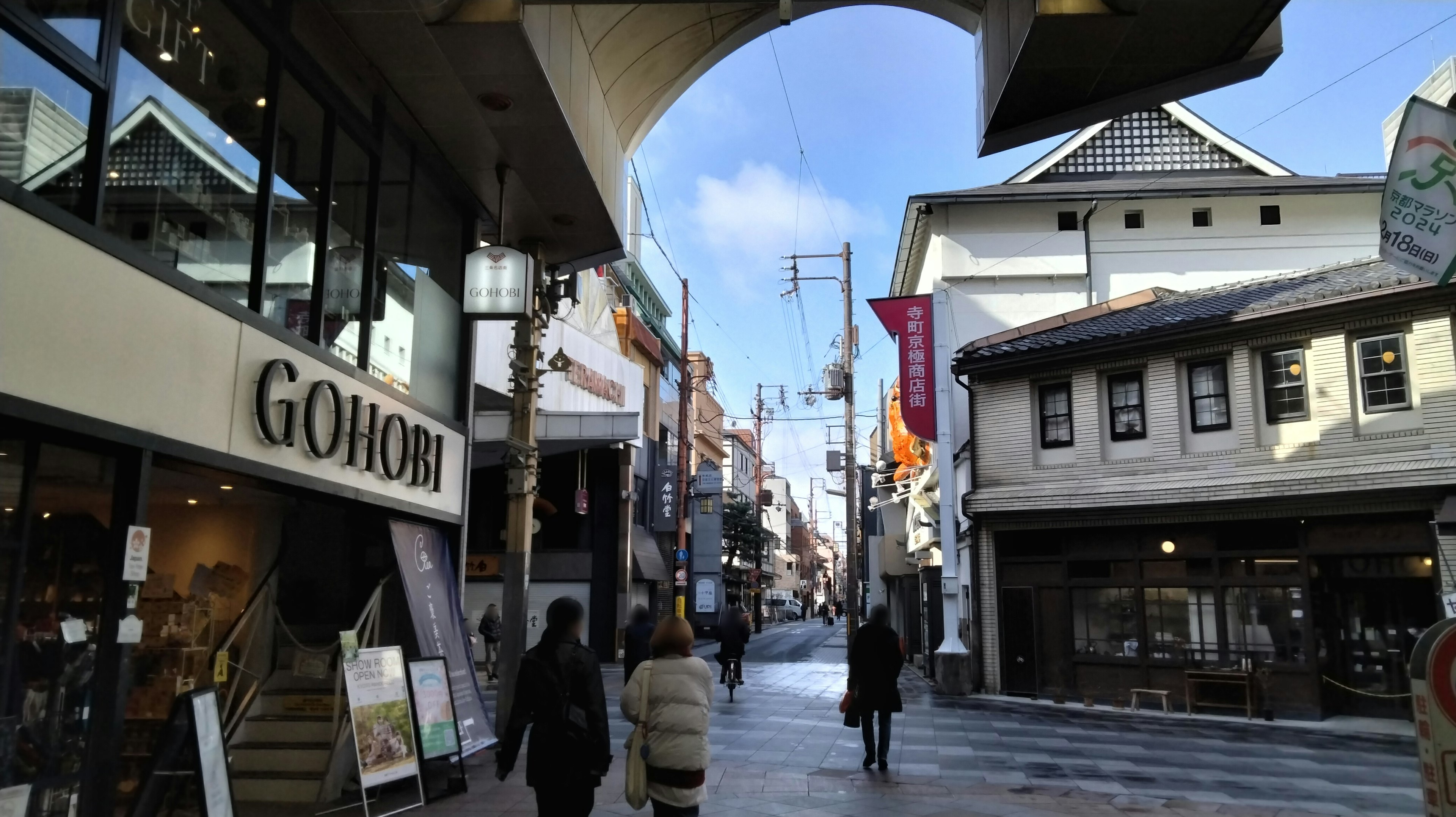 Personas caminando bajo un arco en una calle comercial tranquila