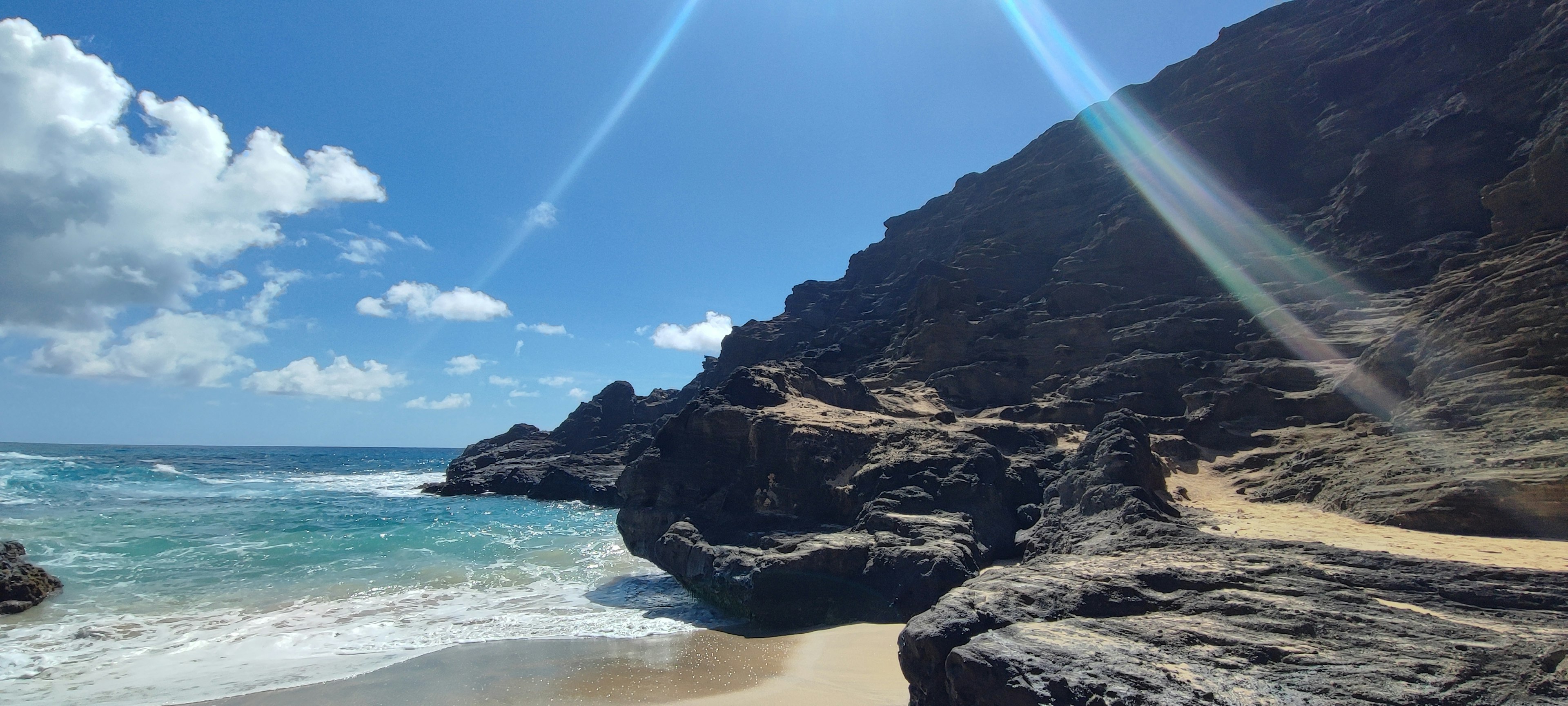 Scenic view of a beach with blue ocean and rocky cliffs under a bright sky