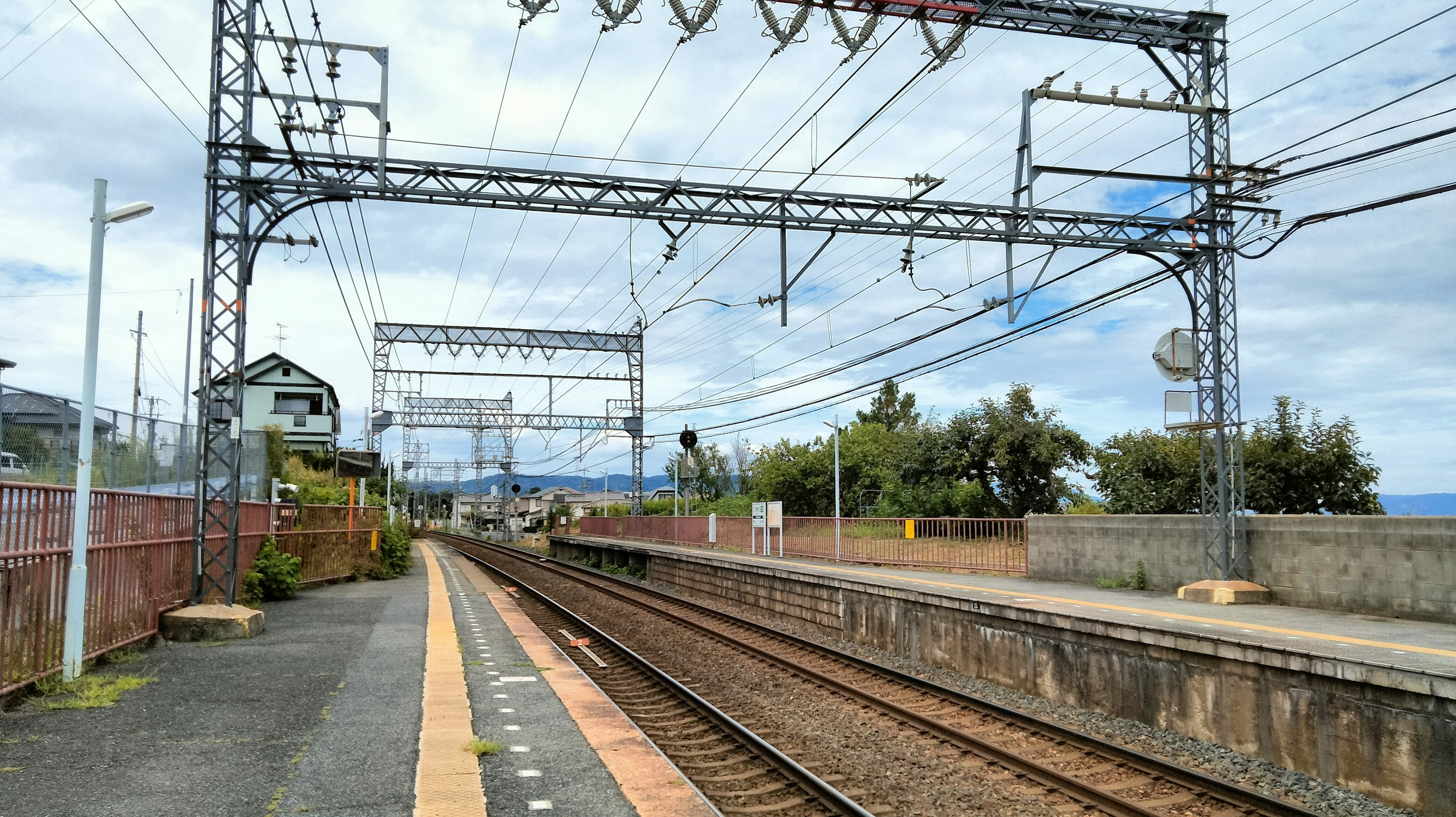 Vista de una plataforma de estación de tren con rieles y cables aéreos