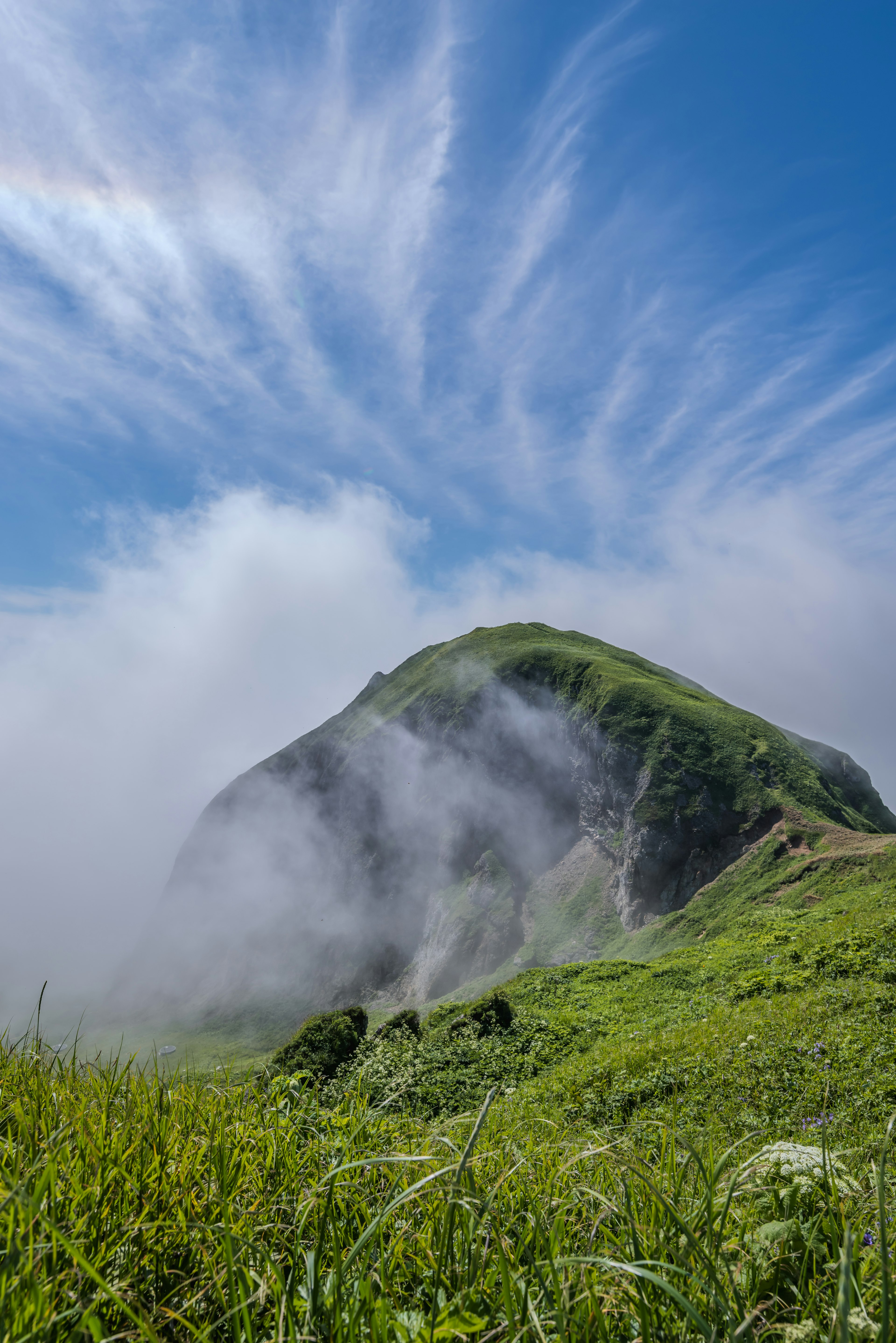 山景与蓝天和云朵 绿色草原在山顶下方的雾中延伸