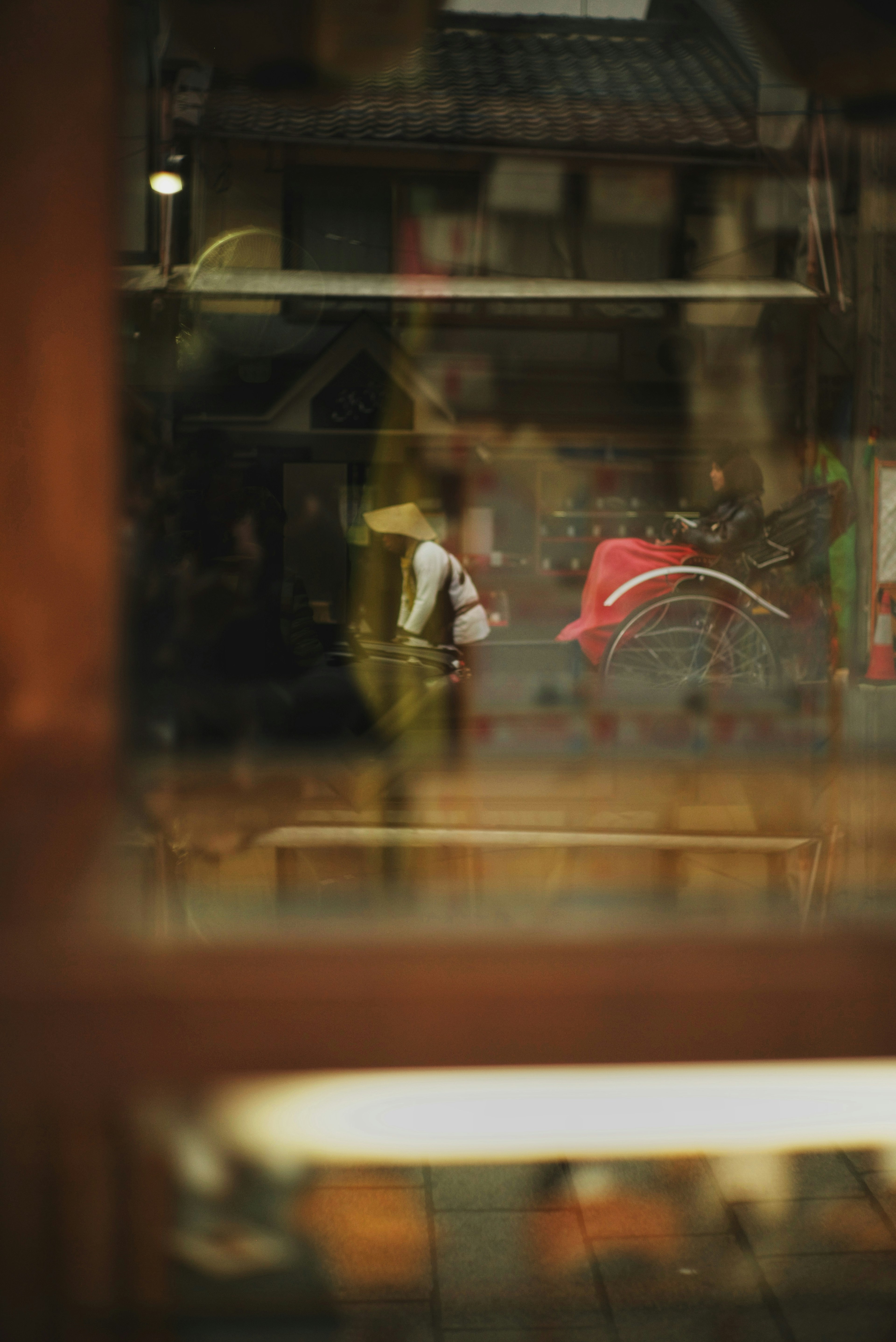 Escena de calle vista a través de una ventana con una persona que lleva un paraguas rojo