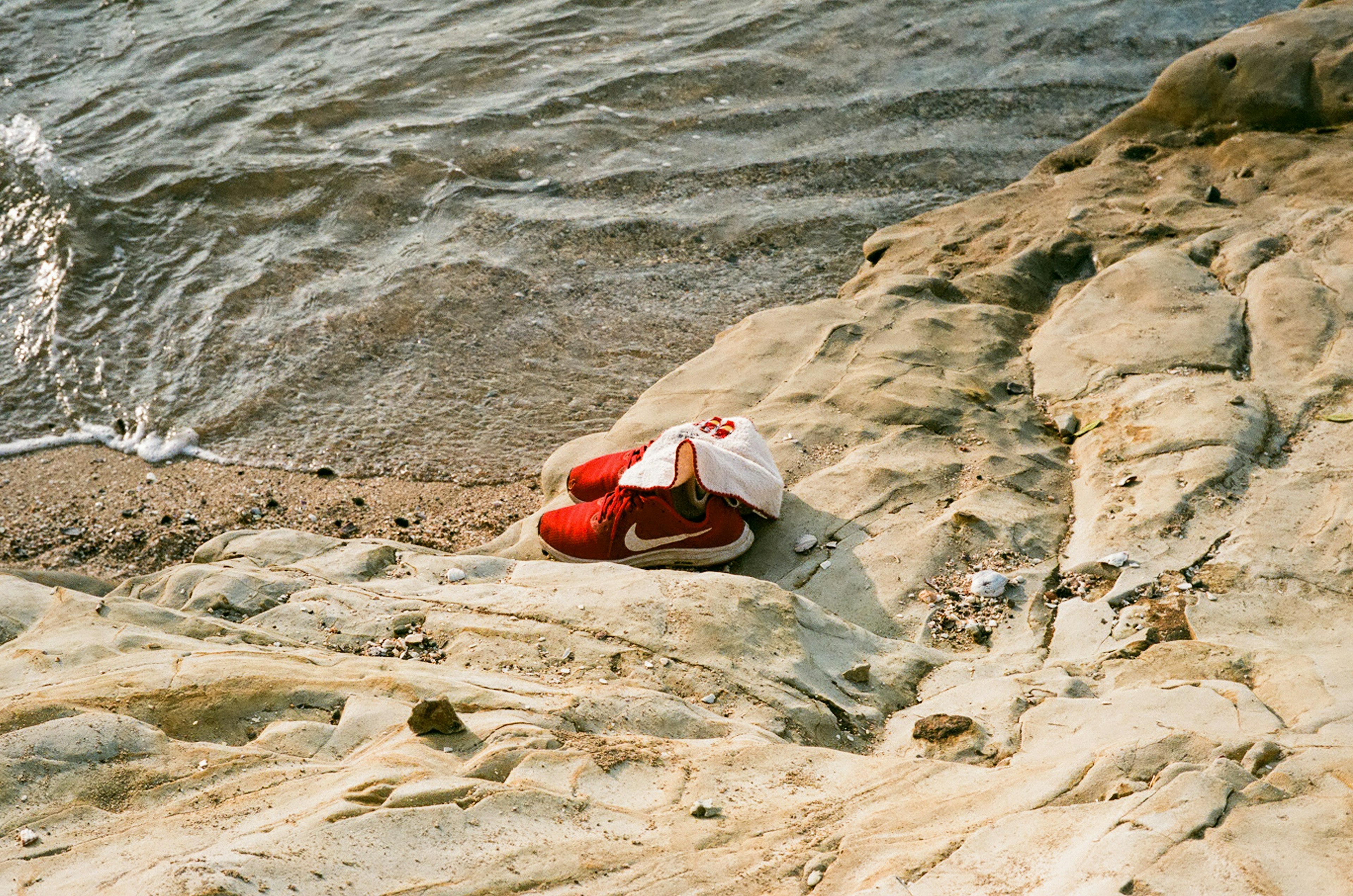 Seseorang berbaring di tepi pantai berbatu dengan sepatu merah