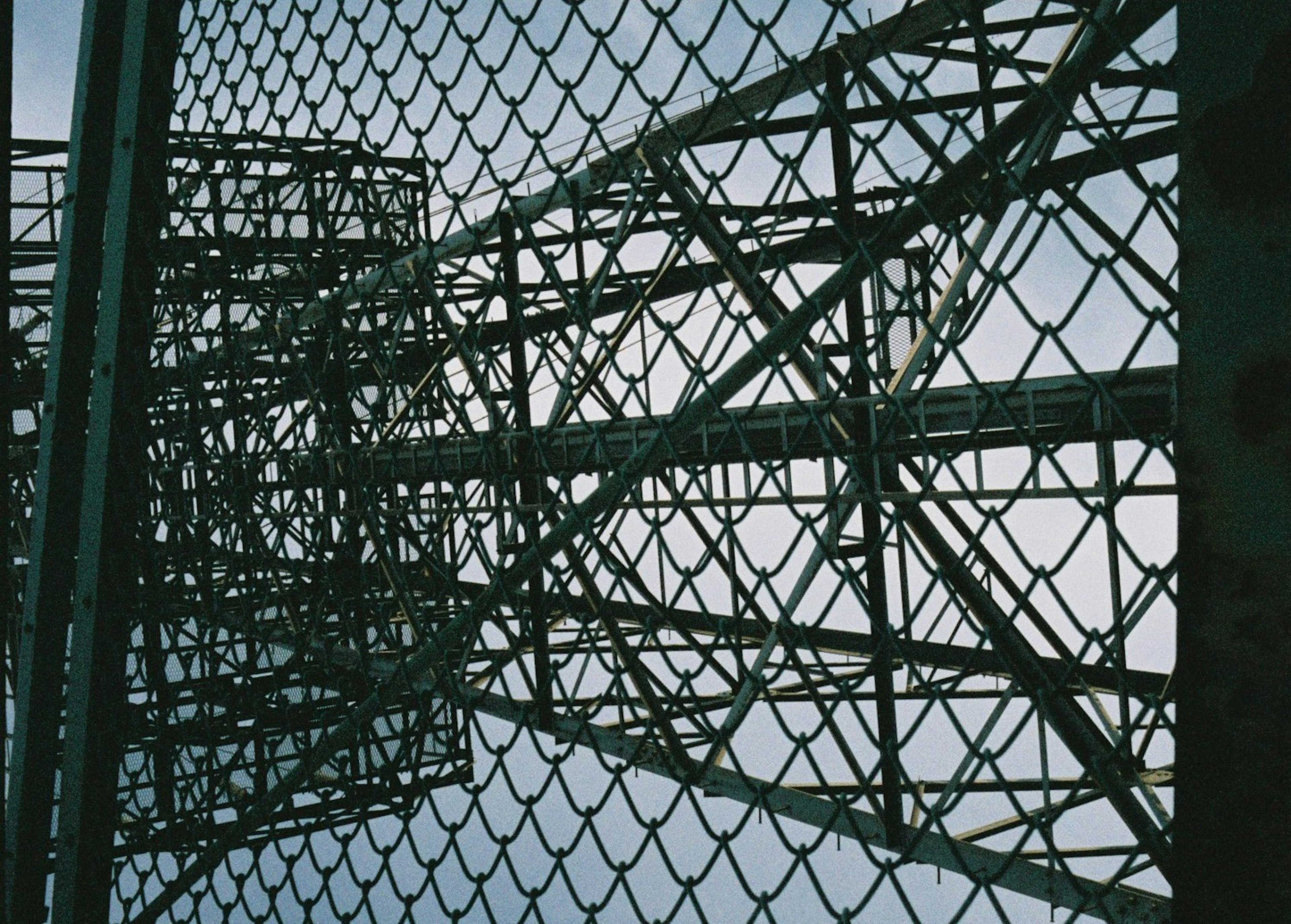 View from below a metal tower showing mesh fence and blue sky