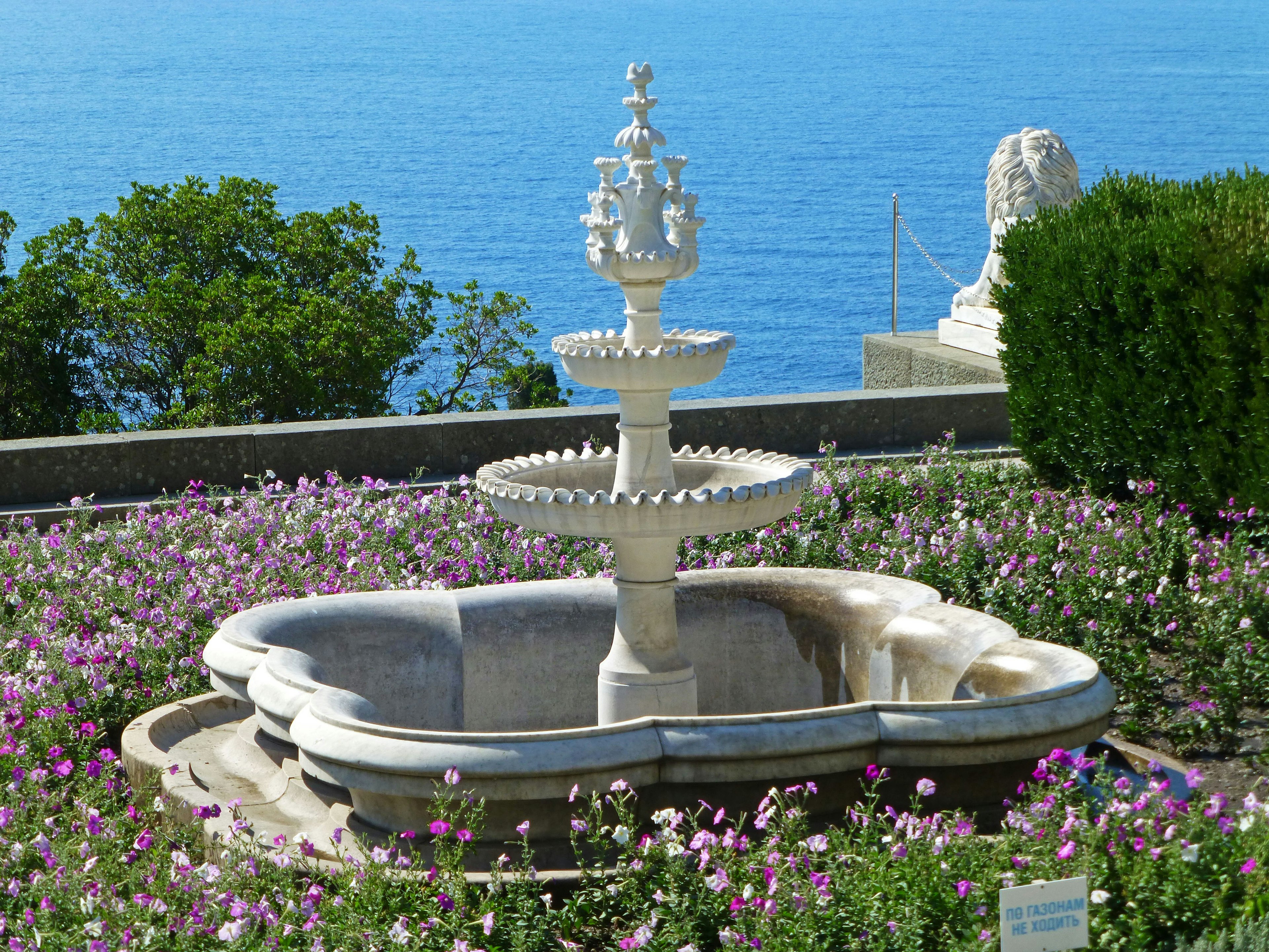 美しい海の景色を背景にした装飾的な石の噴水 周囲には色とりどりの花が咲いている