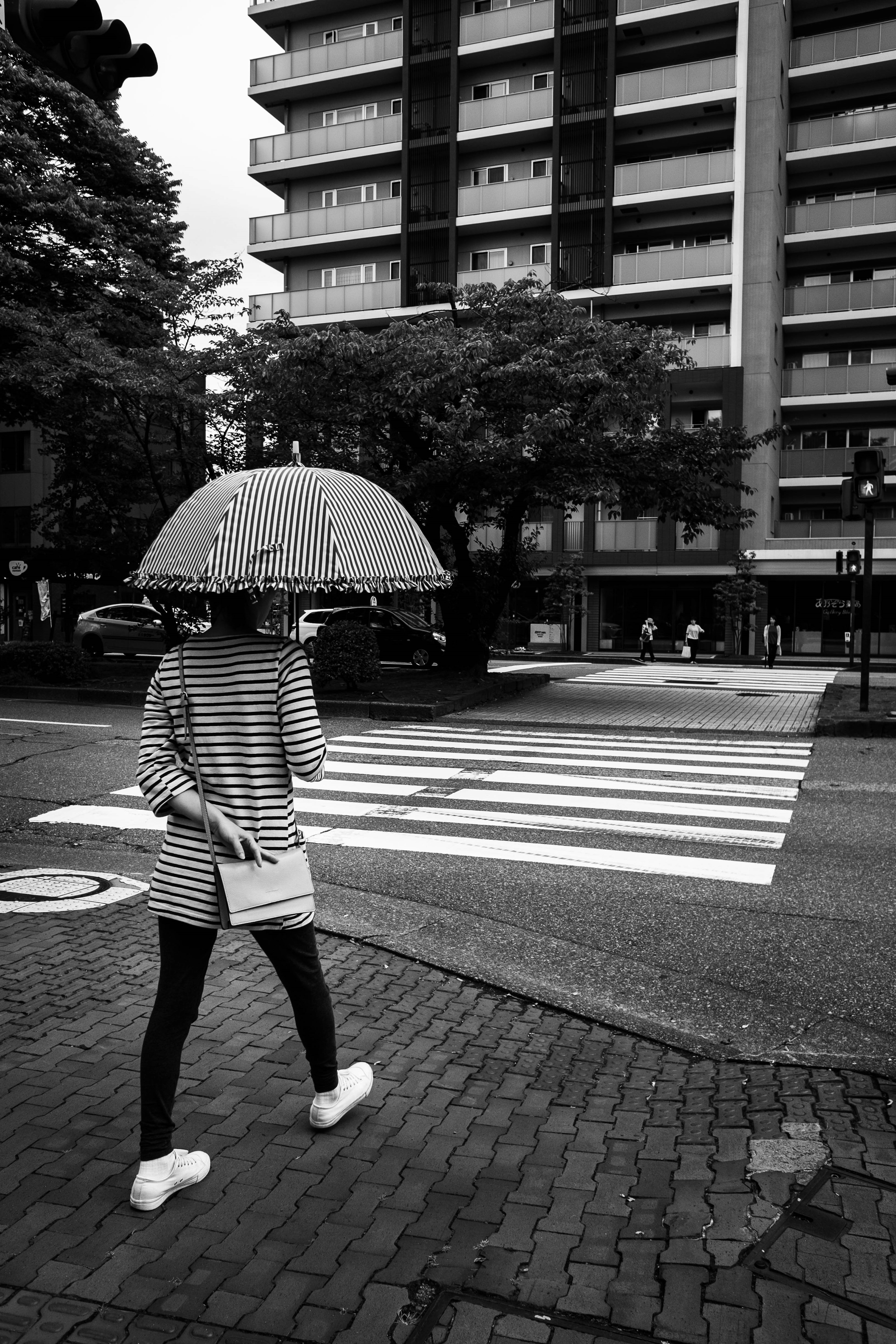 Woman in striped attire holding an umbrella walking across a crosswalk