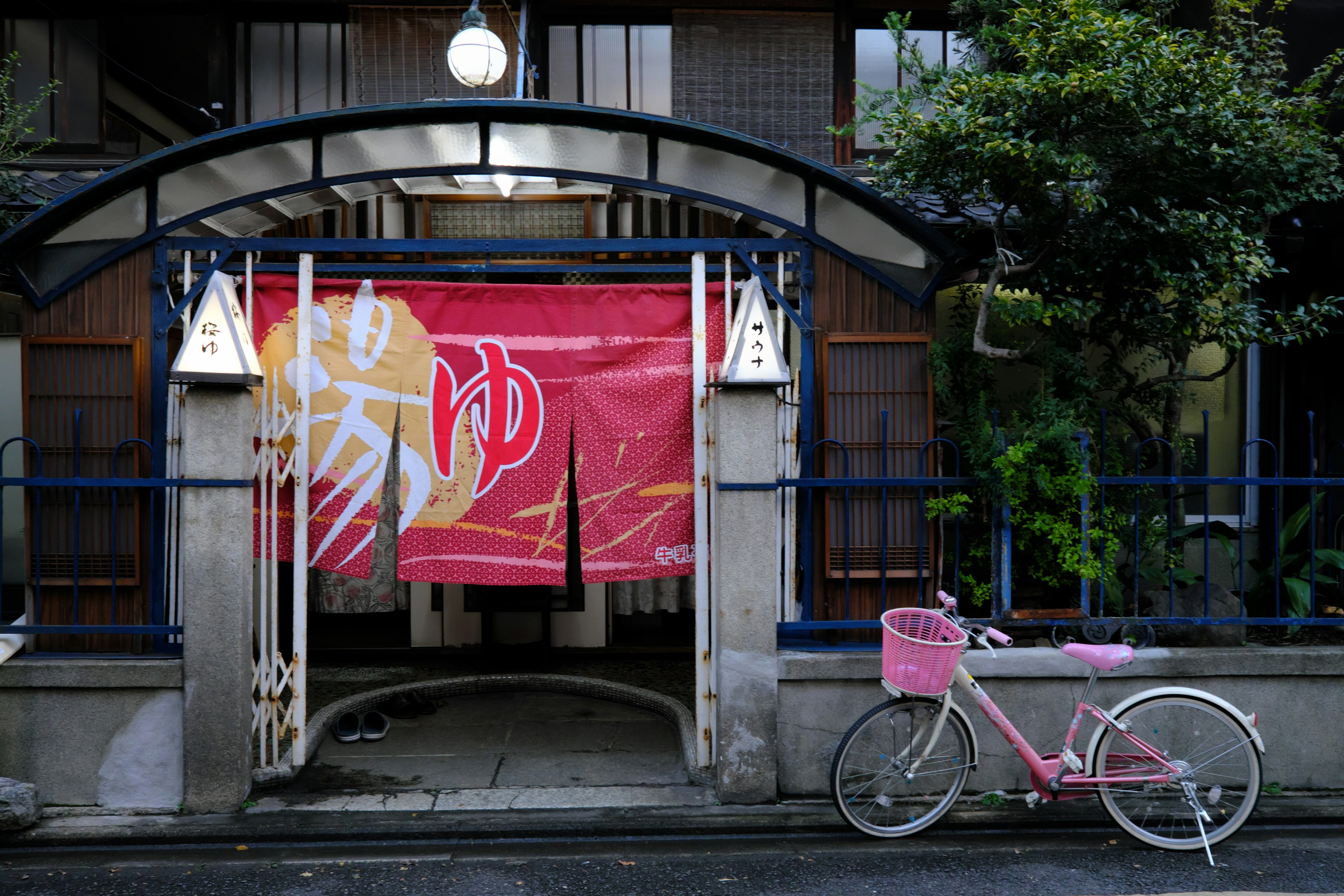 Entrada de un edificio japonés tradicional con una bicicleta rosa y un noren decorativo