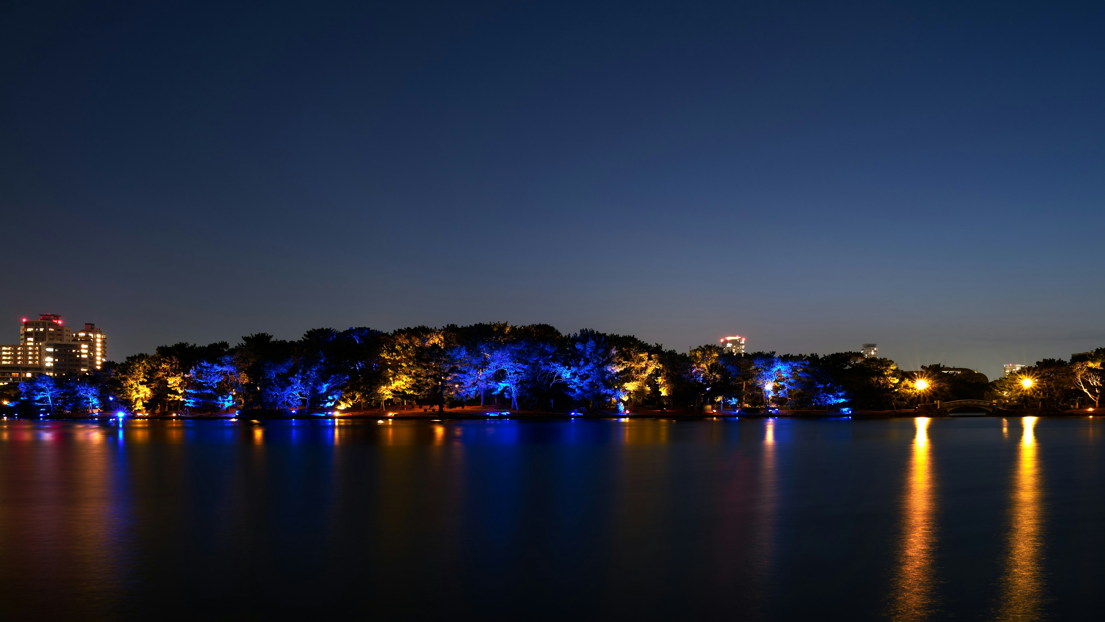 夜の湖に映る青とオレンジのライトが美しい風景