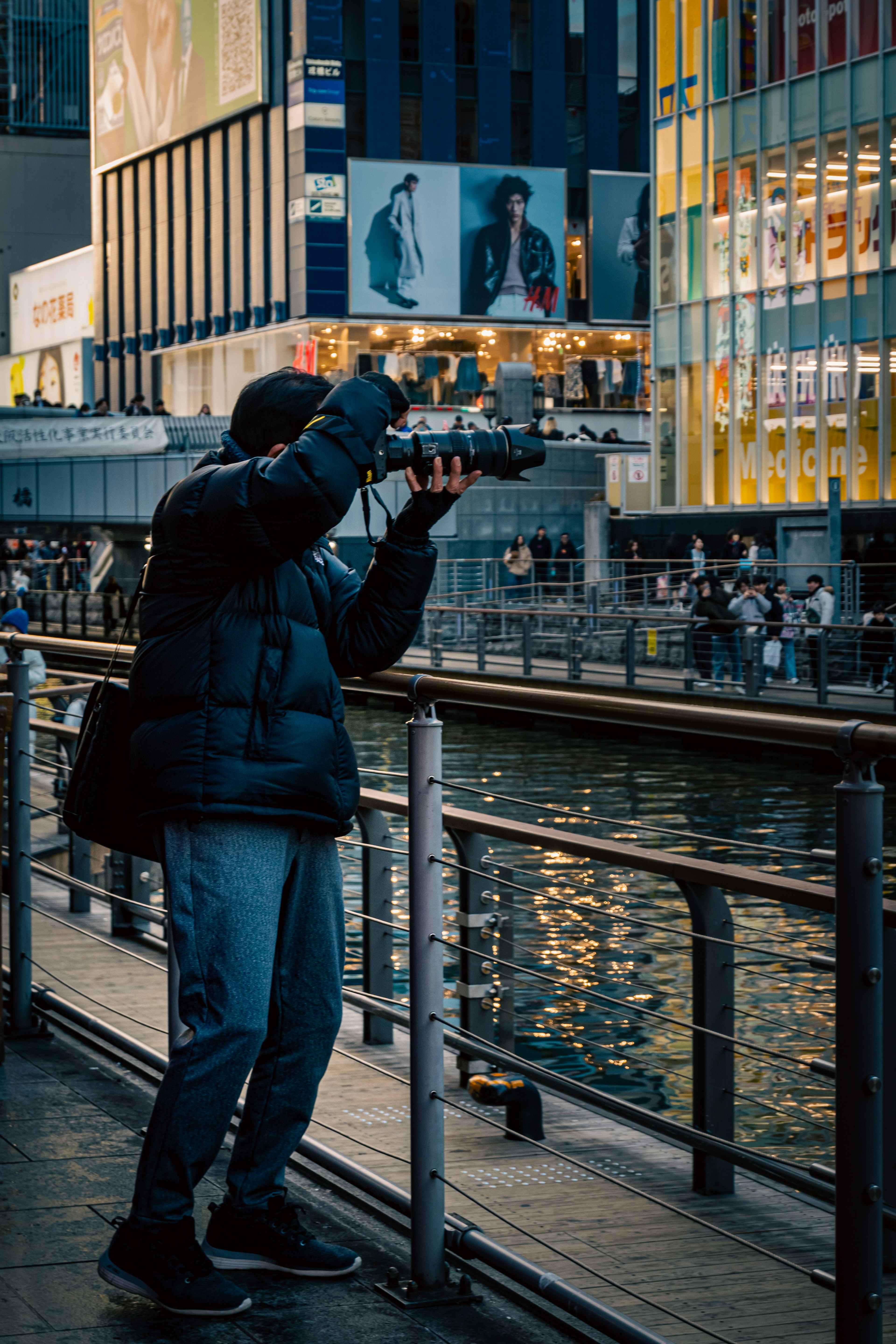 Homme photographiant au bord de l'eau la nuit avec des lumières de la ville