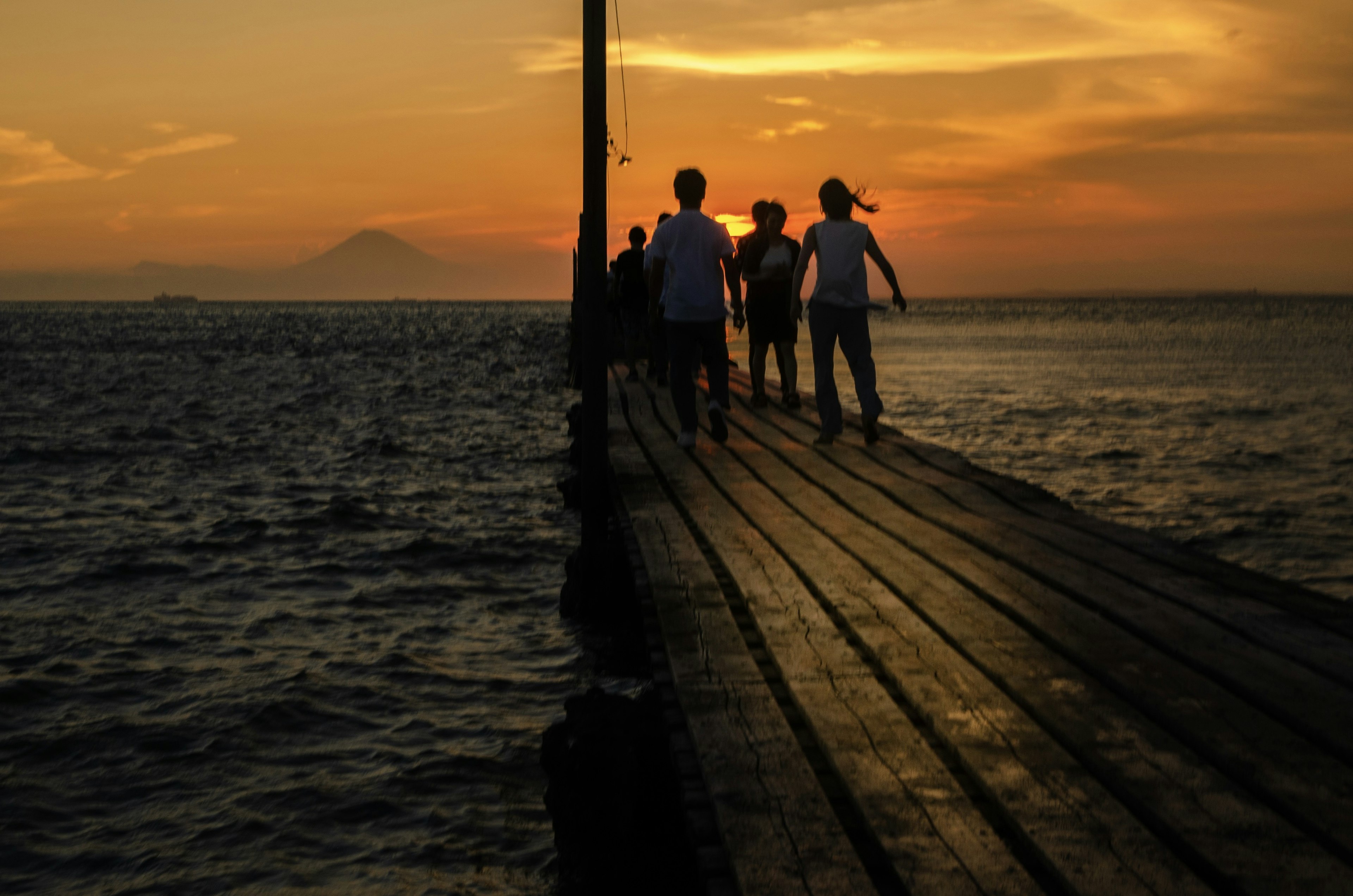 Silhouetten von Menschen, die bei Sonnenuntergang auf einem Steg gehen