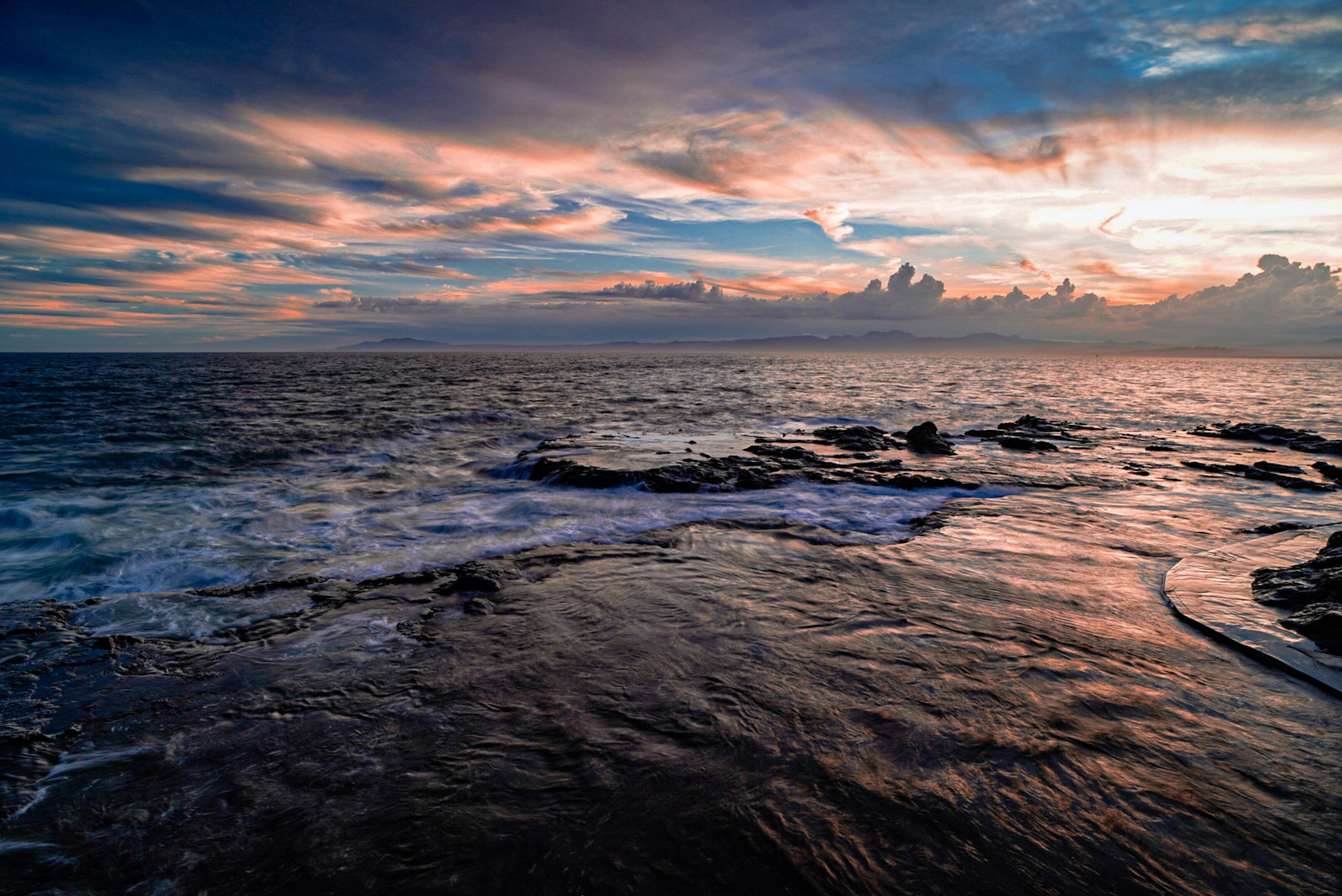 Stunning sunset over the ocean with waves crashing on rocky shore