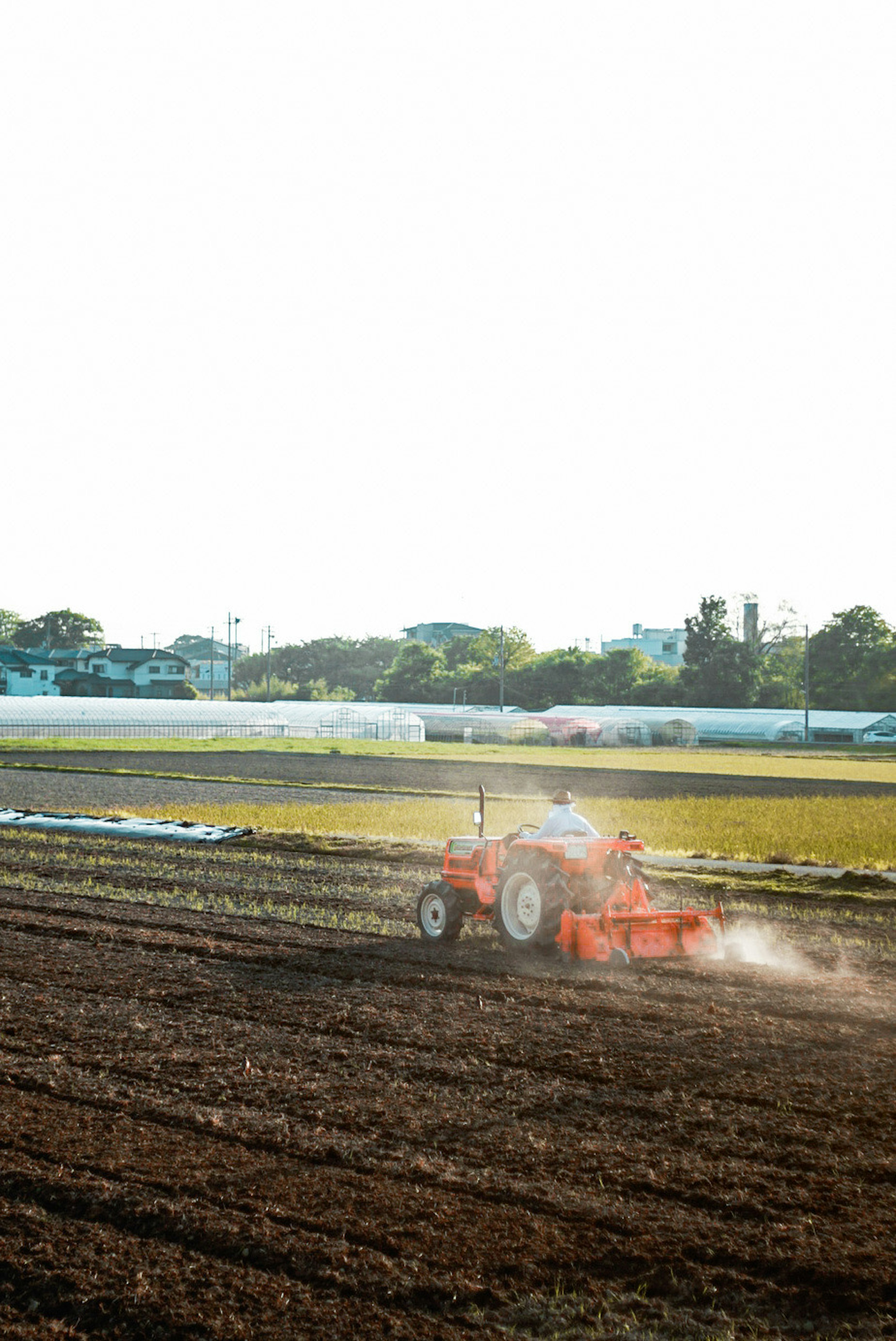 Ein orangefarbener Traktor pflügt ein Feld unter einem hellen Himmel