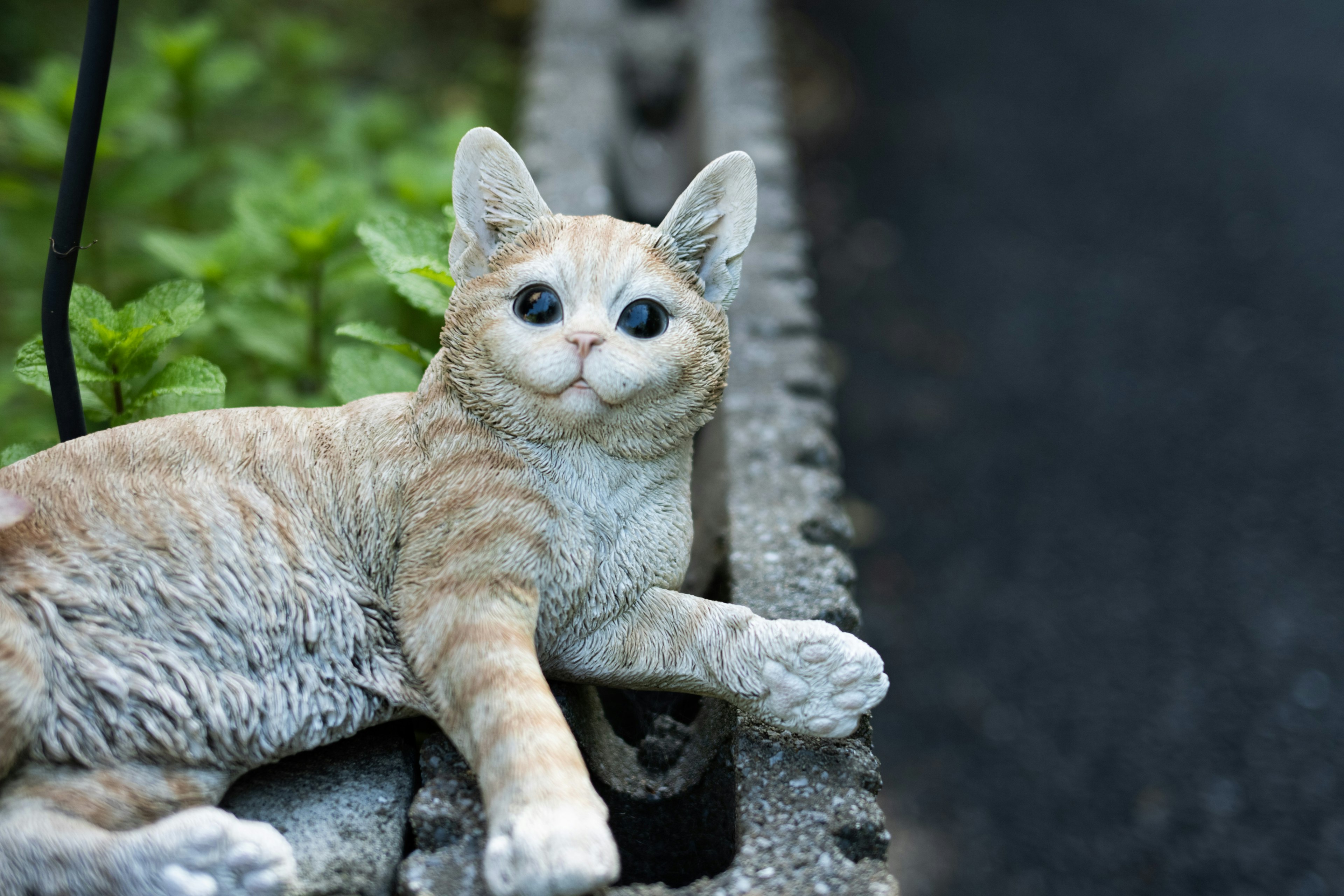 一个现实主义的猫雕像躺在绿色植物旁边