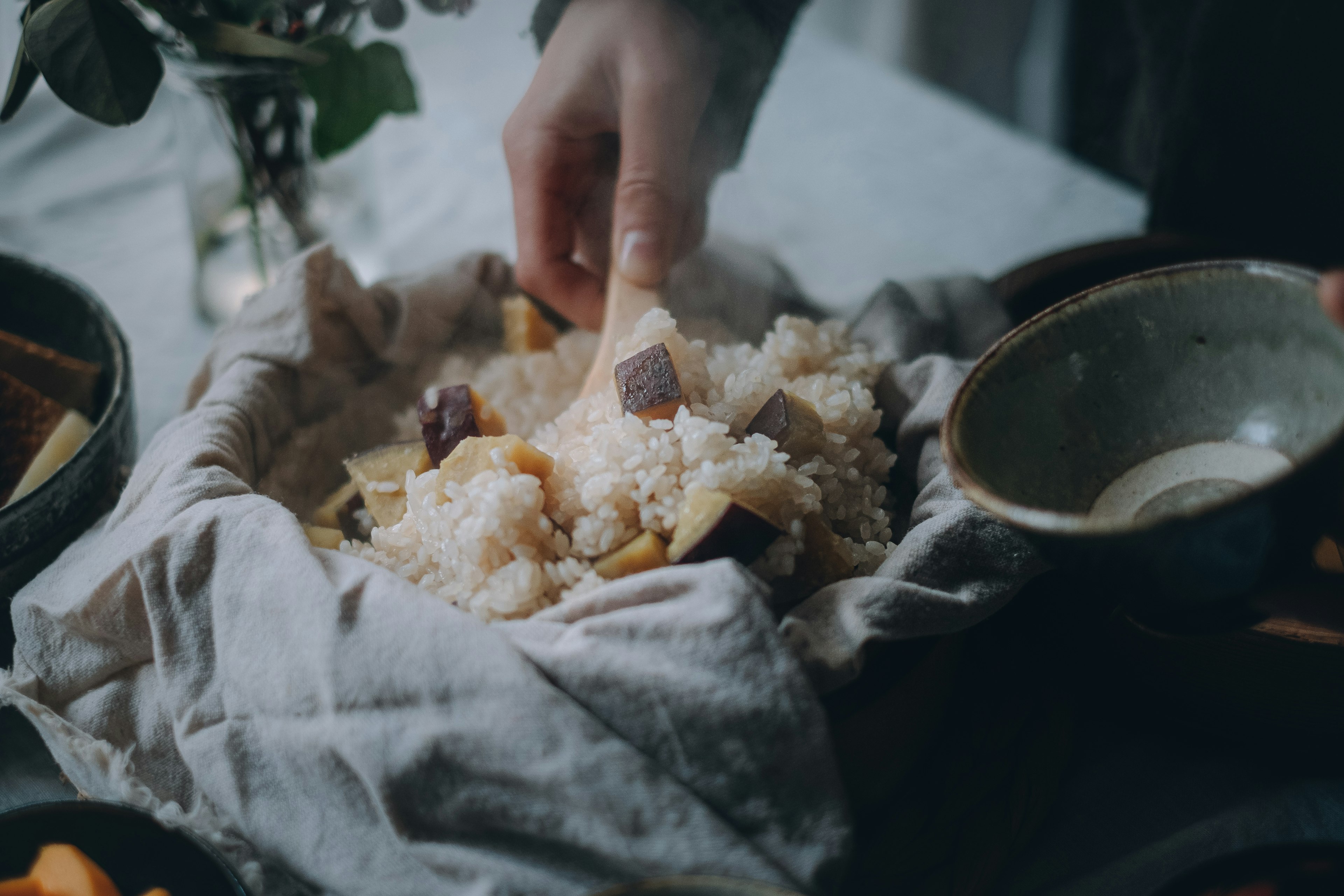 A person picking up food with their hand from a cloth-covered dish on a table