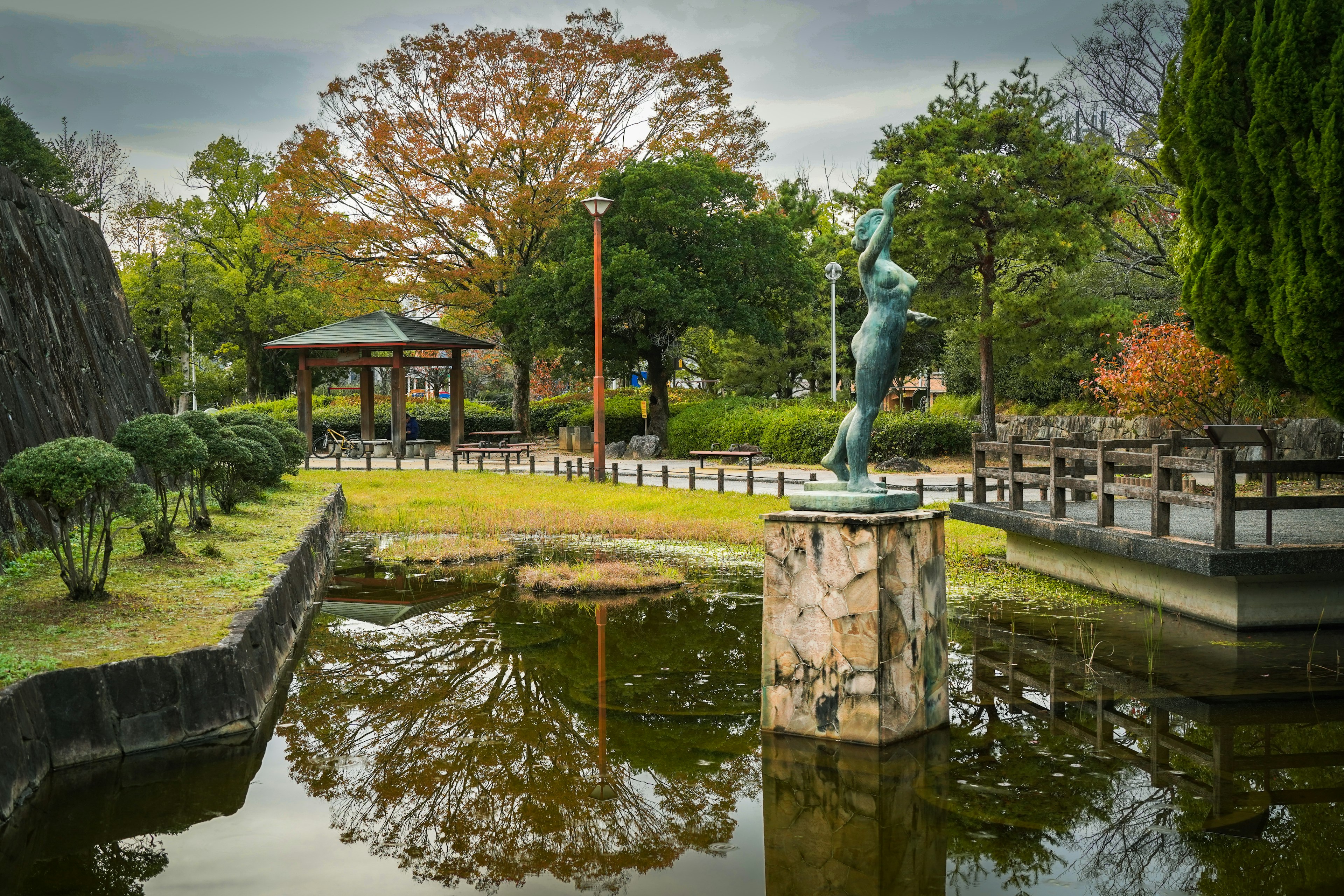 公園の池に立つ彫刻と周囲の美しい景色