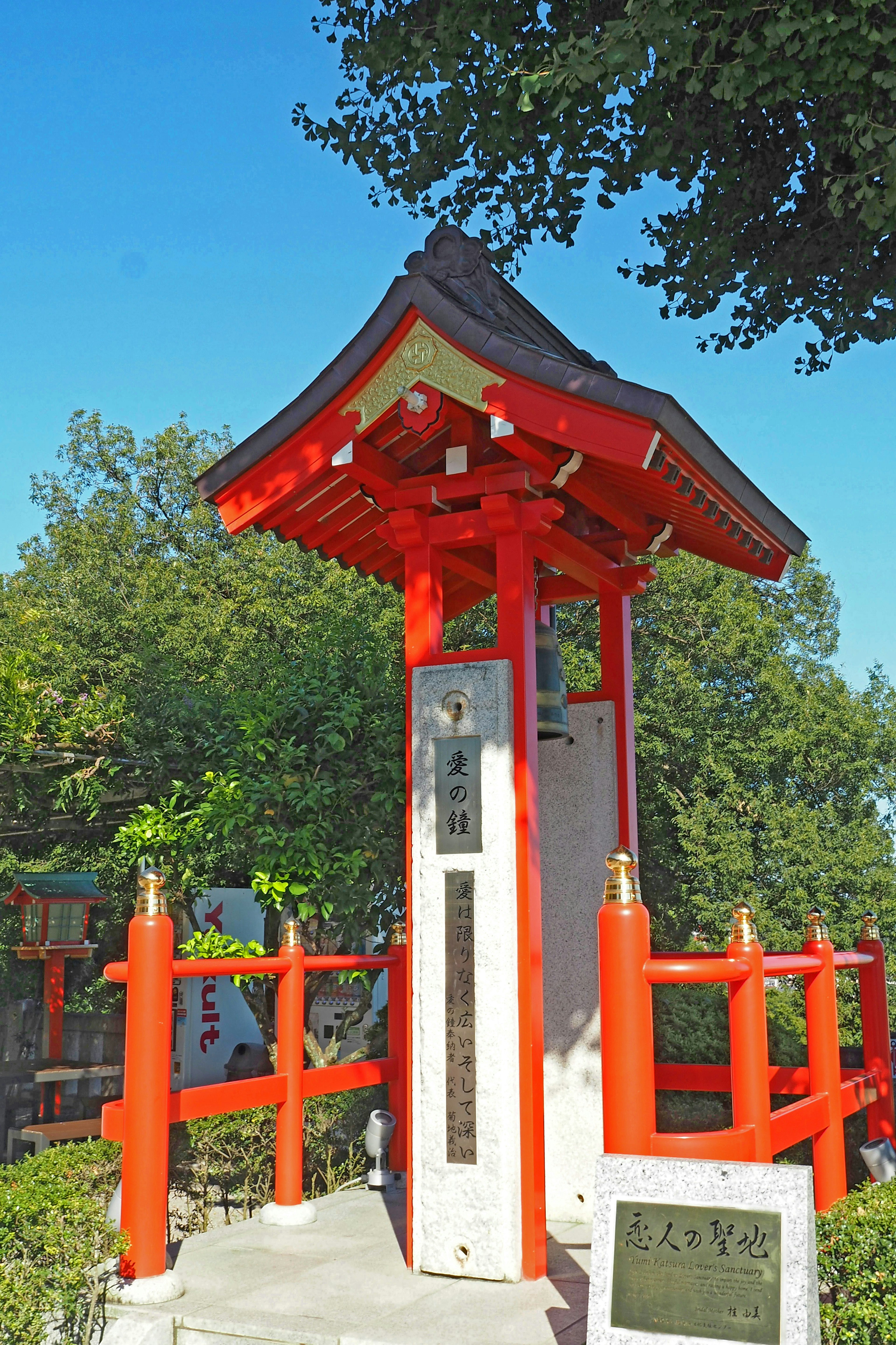 A small shrine-like structure with a red roof and white columns set in a green environment