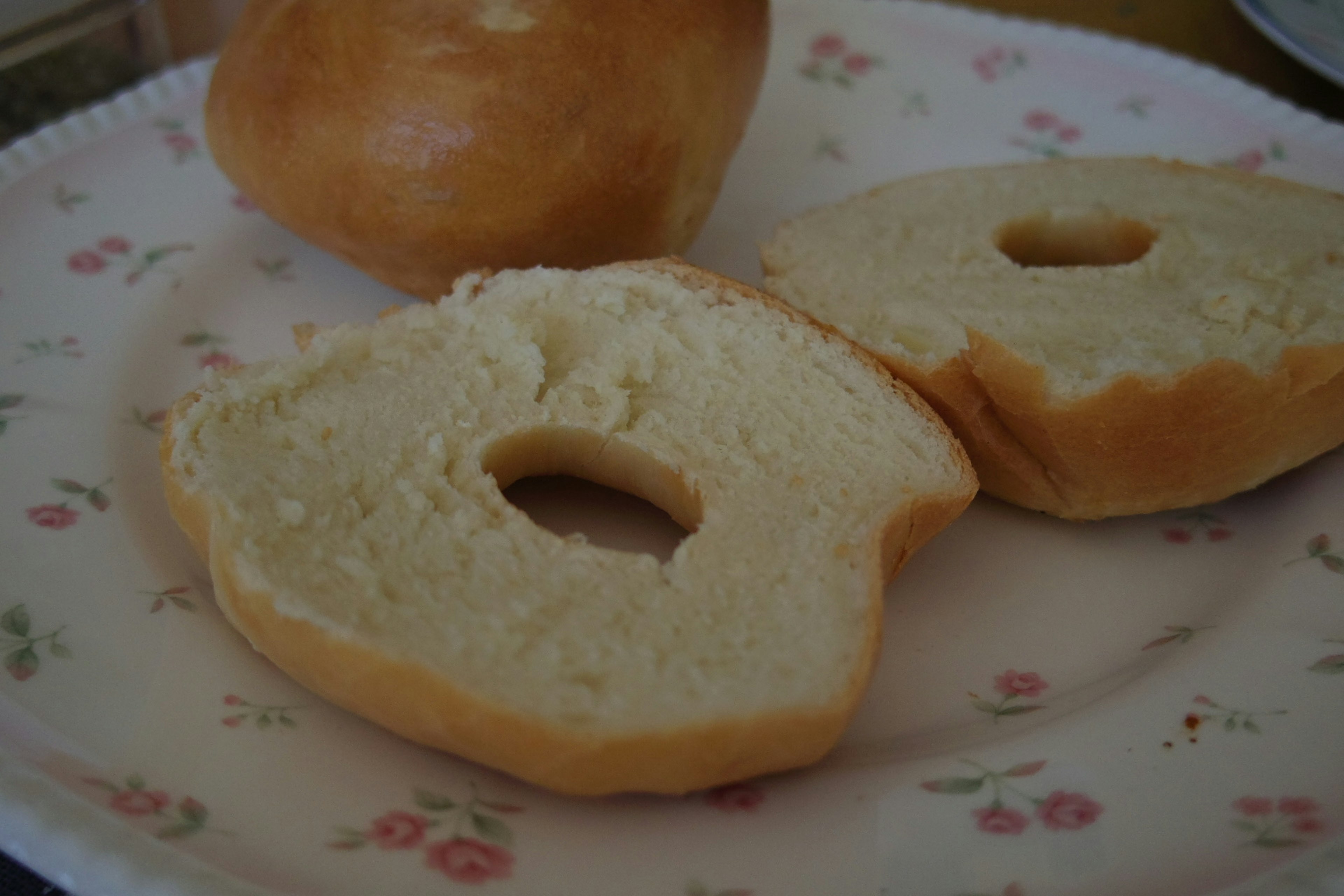 Zwei Scheiben eines Donuts mit Loch auf einem blumigen Teller und ein ganzer Donut im Hintergrund