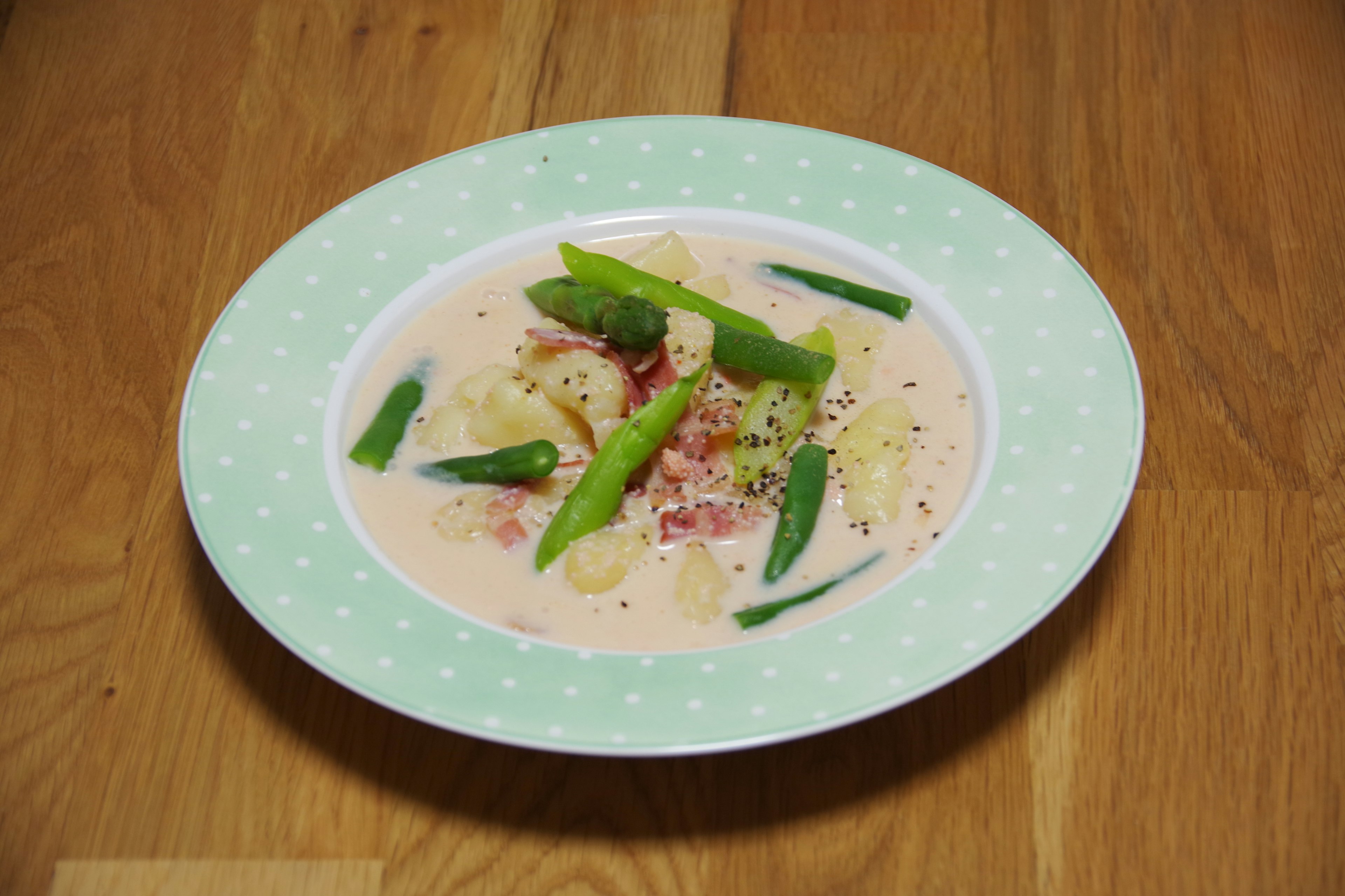 A dish of pasta in cream sauce topped with green asparagus and ham