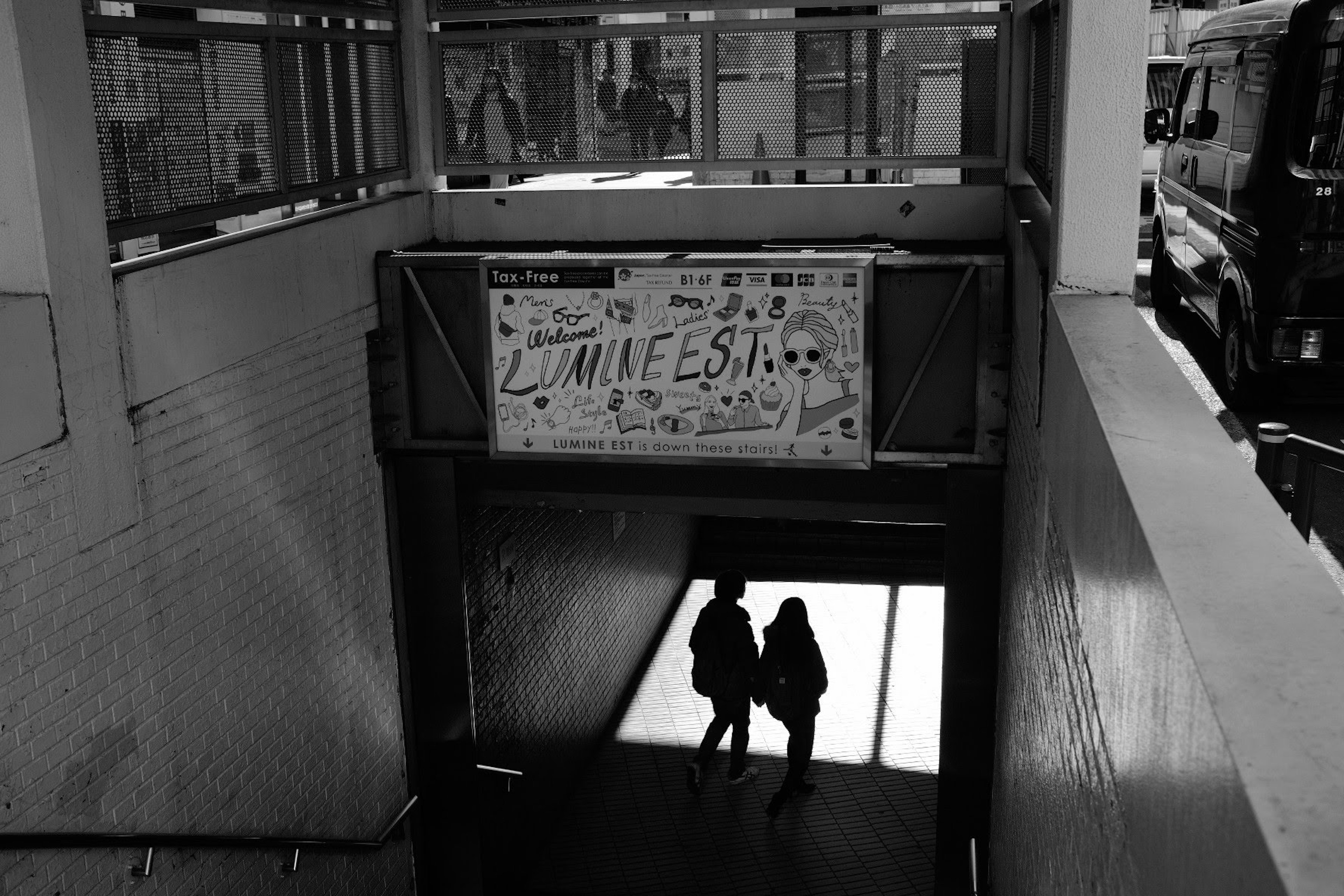 Deux silhouettes à l'entrée d'un passage souterrain avec un panneau coloré