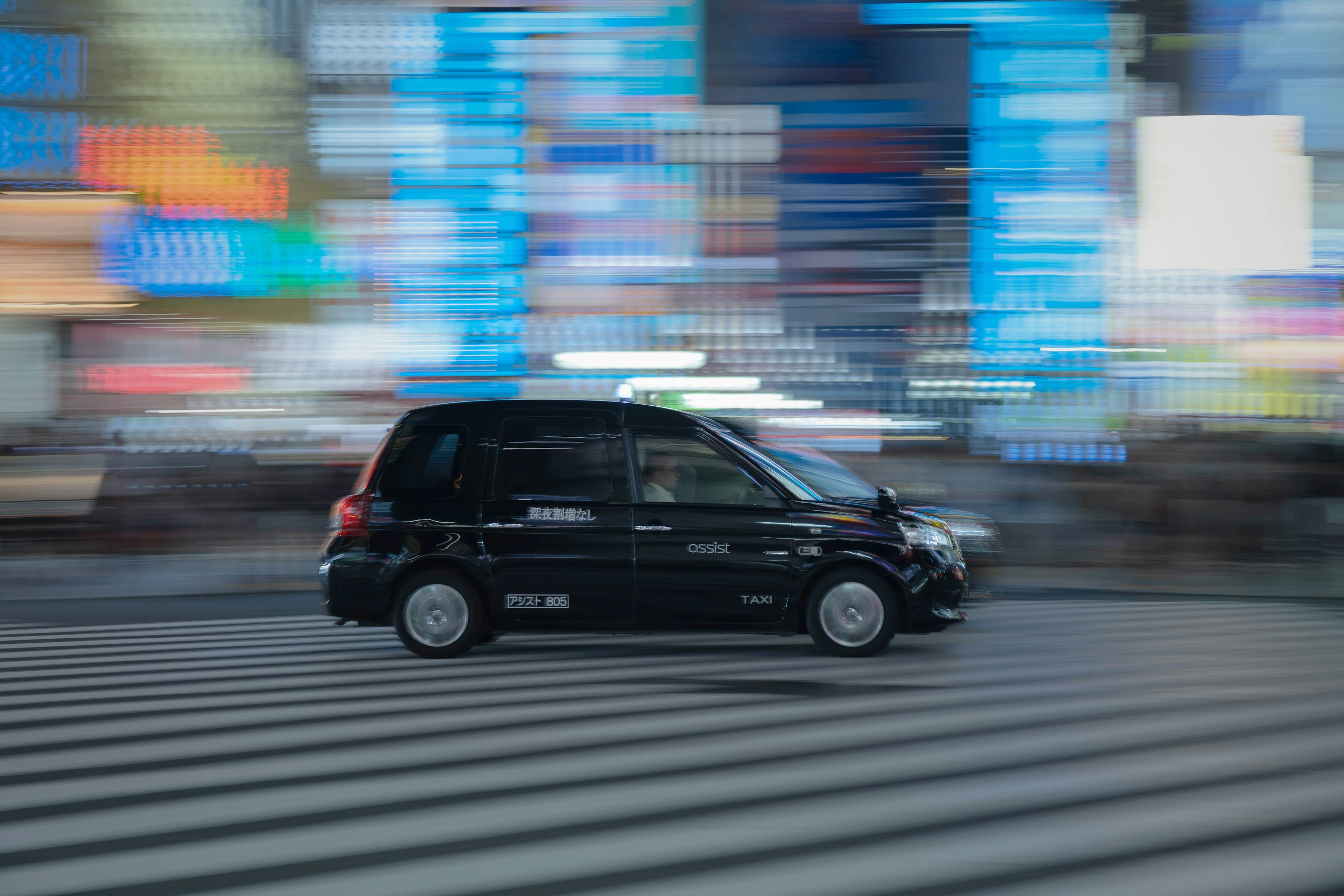 Auto nera che attraversa un passaggio pedonale con luci al neon colorate sullo sfondo