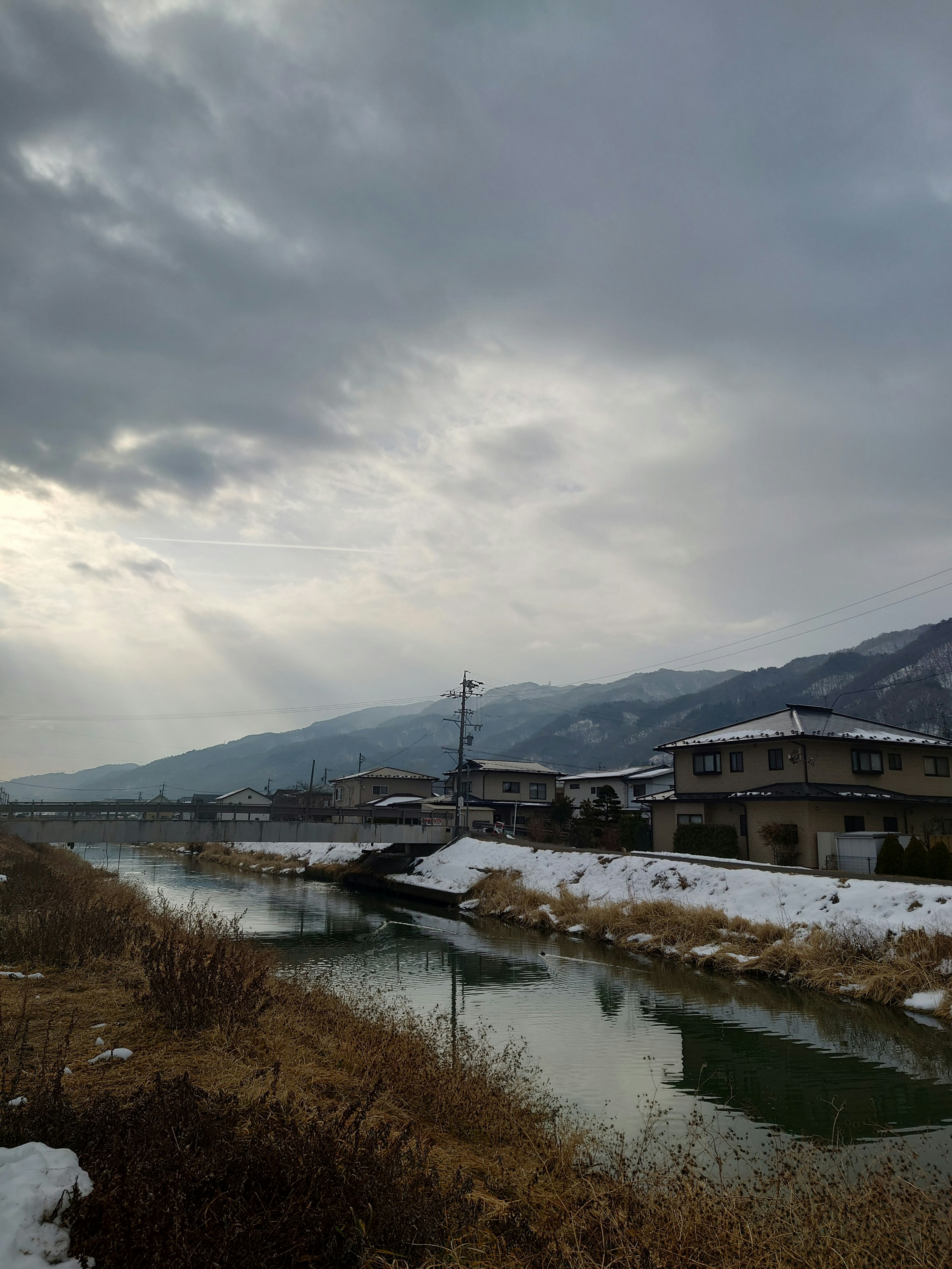 Maisons le long d'une rivière enneigée avec des montagnes en arrière-plan